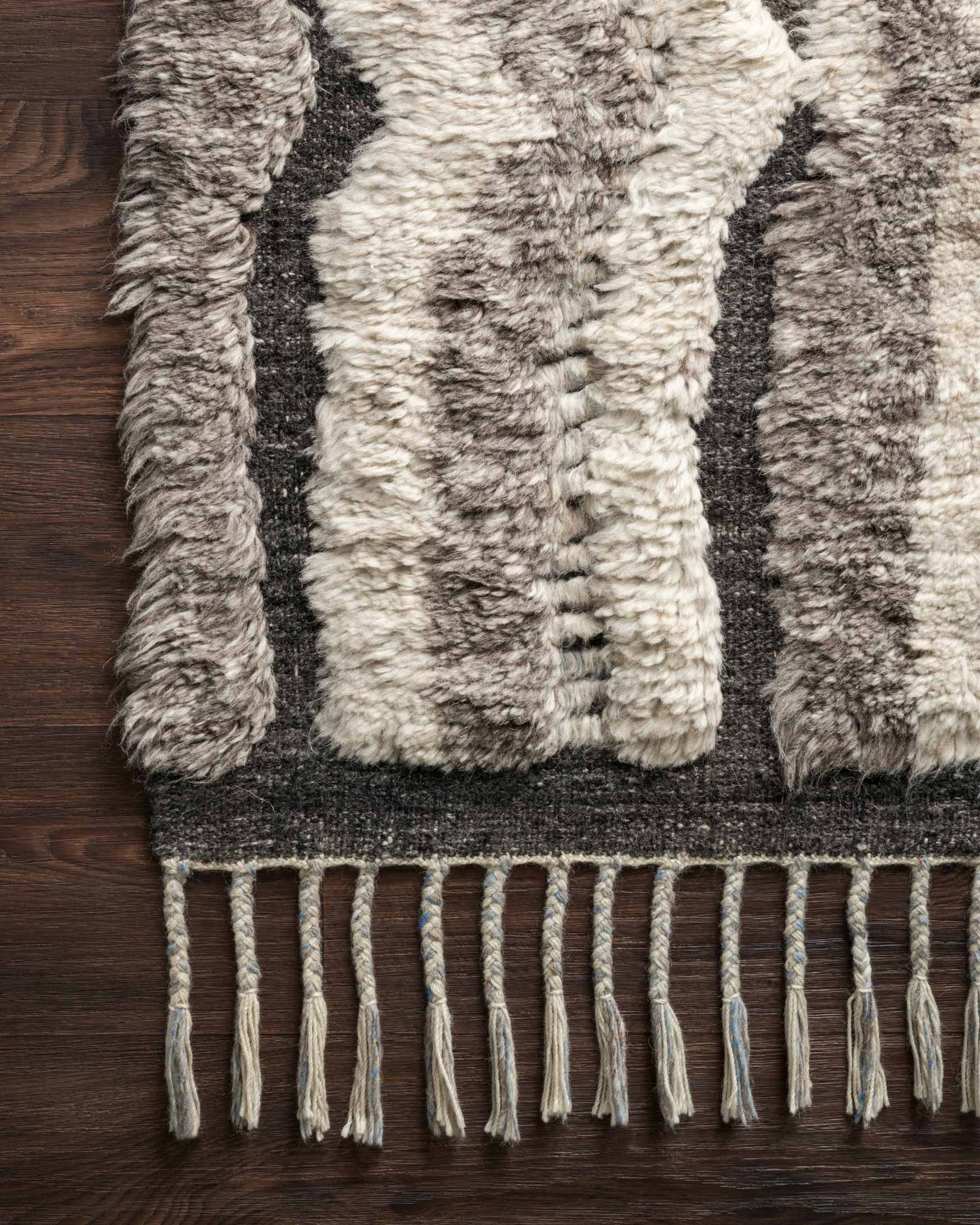Hand-knotted rug close-up with textured pile, charcoal-and-stone keyhole motif, fringe edge