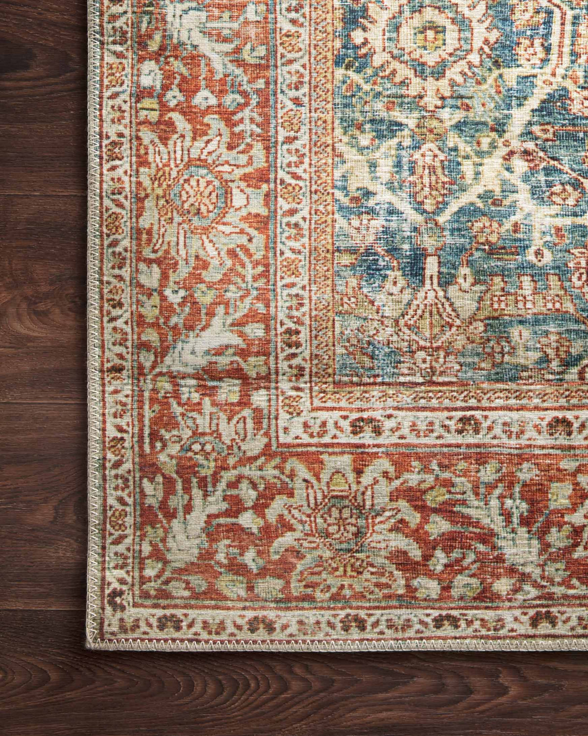 Top corner of traditional rug on dark wood floor, blue field with rust accents.