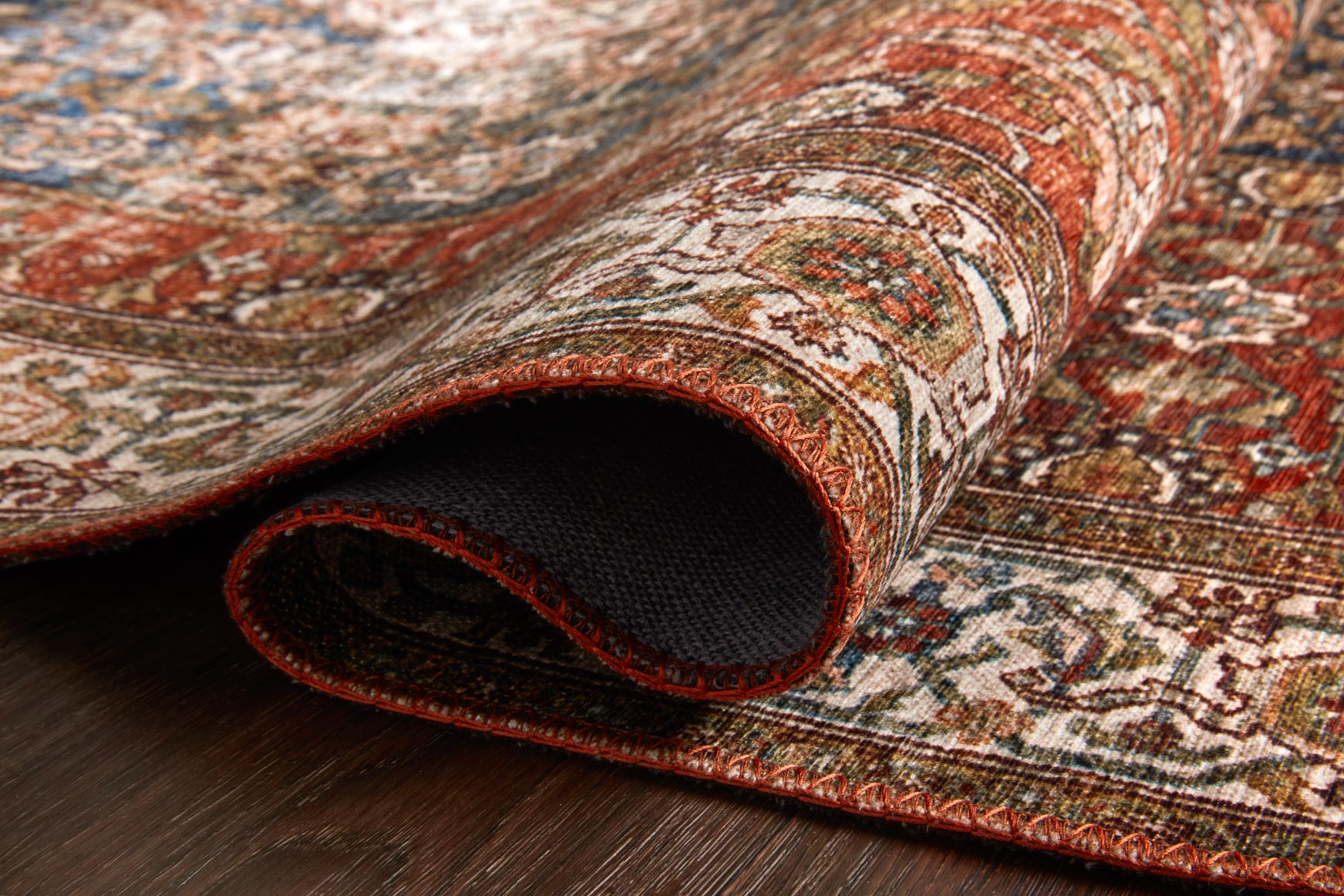 Rolled traditional power-loomed rug showing patterned surface and dark underside backing.