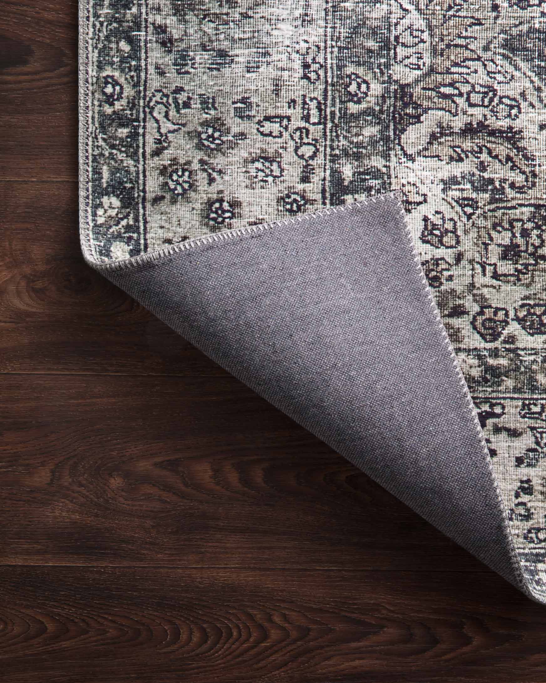 Traditional power-loomed rug edge lifted to show underside in taupe and stone coloring