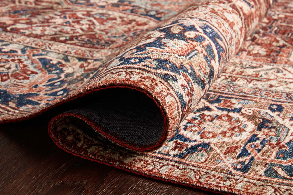 Rolled edge of red and navy rug showing underside and tightly bound trim.