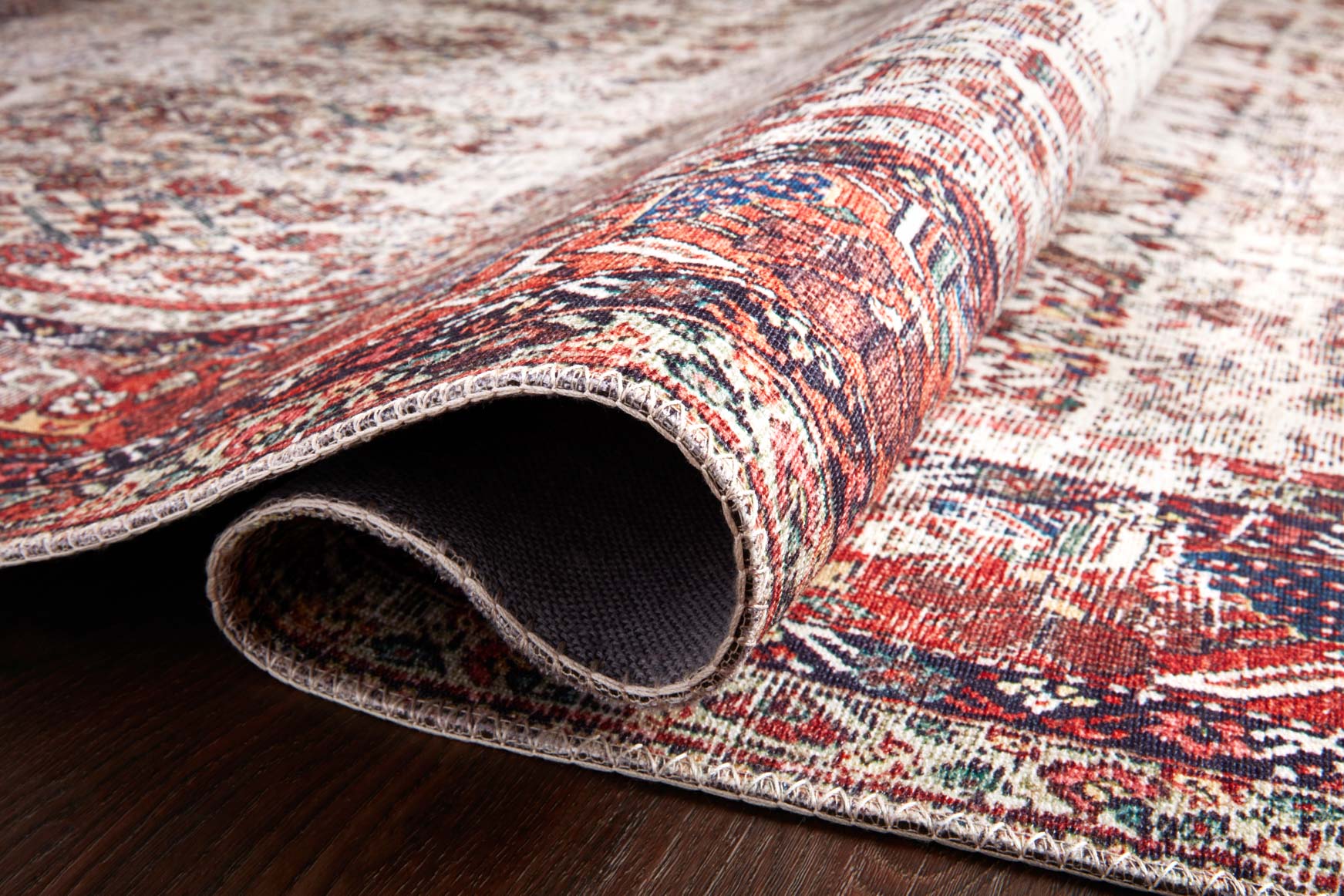 Rolled rug edge showing multicolor pattern and woven backing on ivory ground.