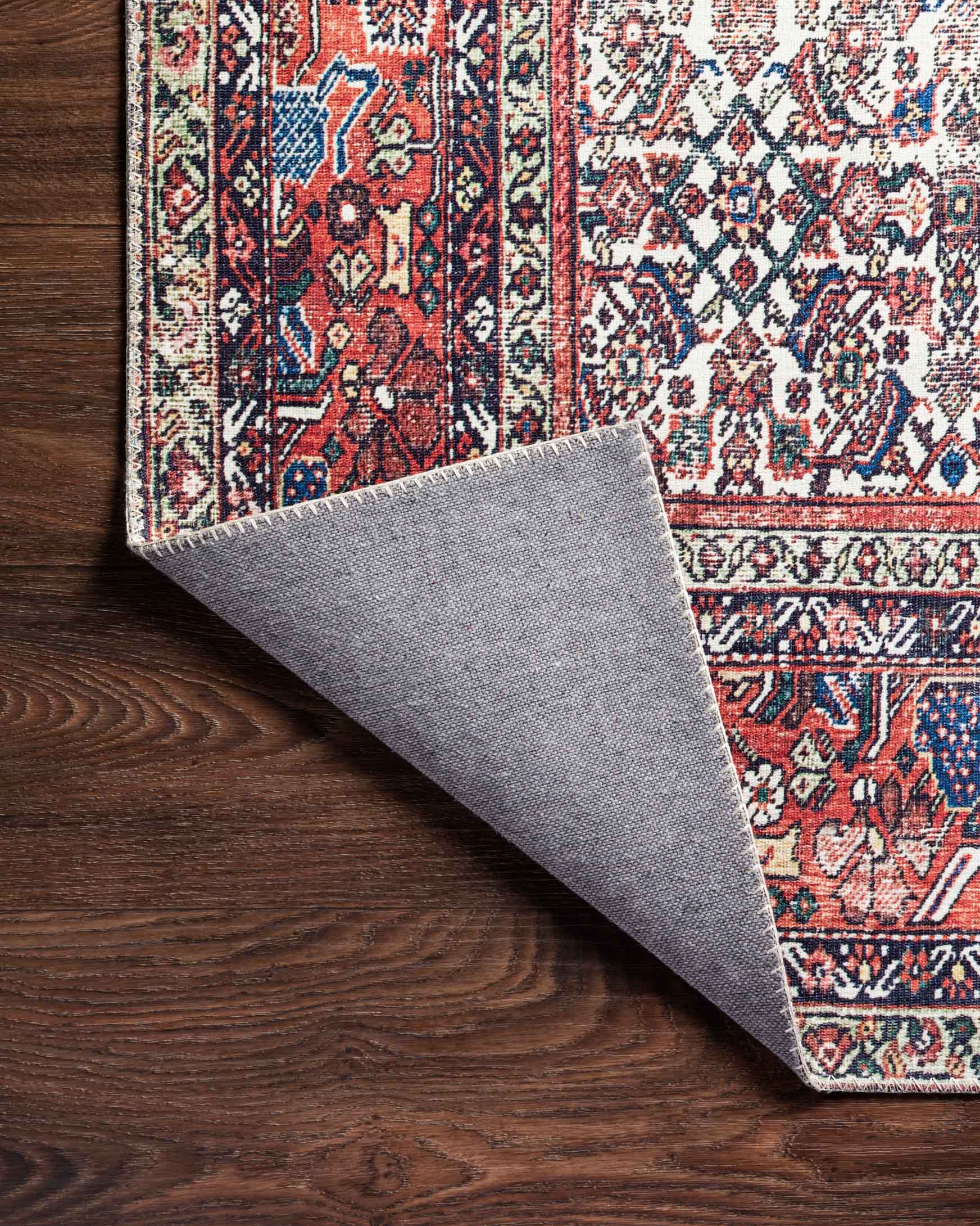 Folded rug corner showing gray backing, with patterned ivory and brick front.
