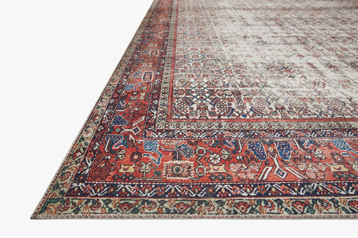 Corner of ivory and brick rug with ornate border and multicolor geometric motifs.
