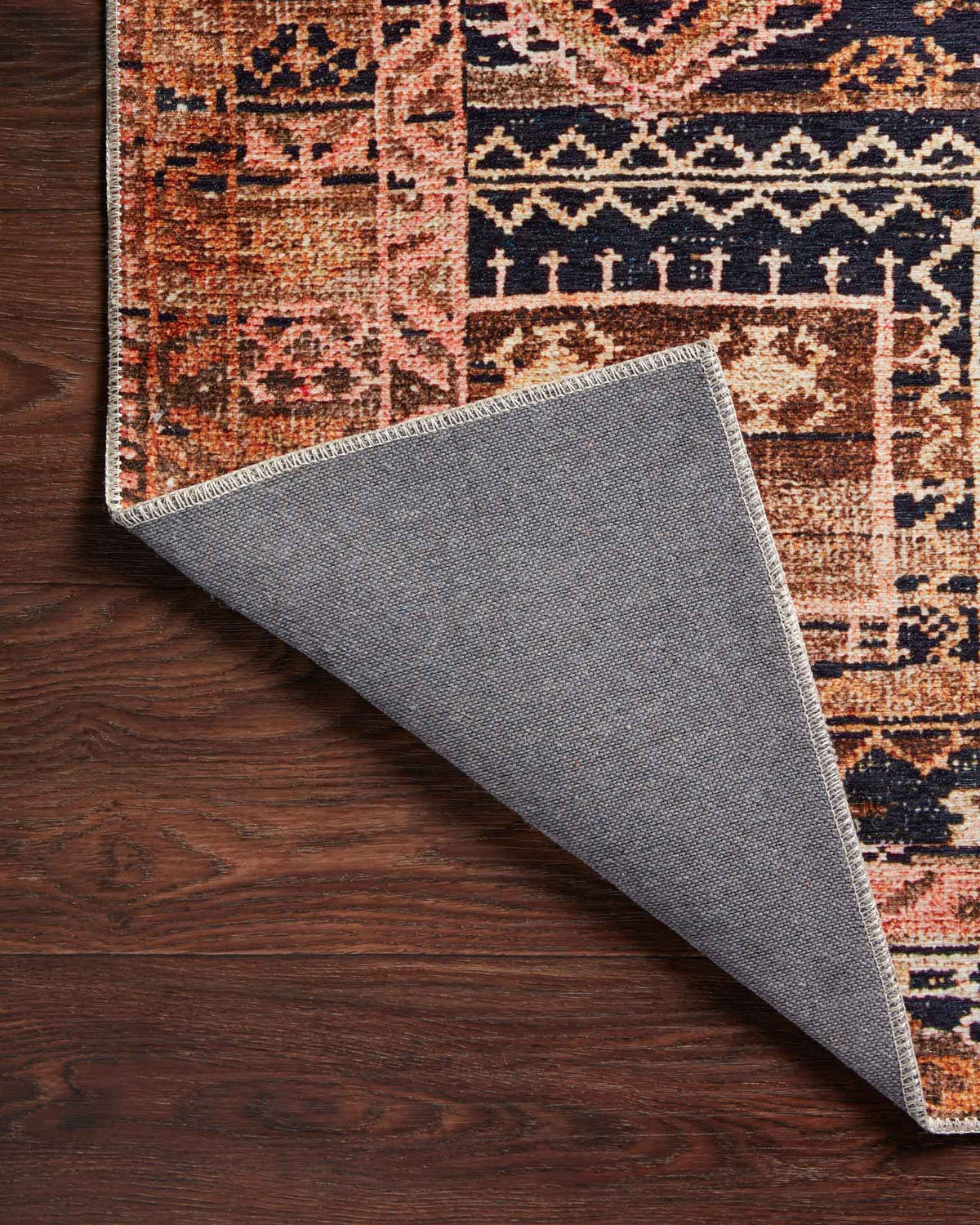 Mocha and blush rug lifted corner revealing gray backing and stitched edge.