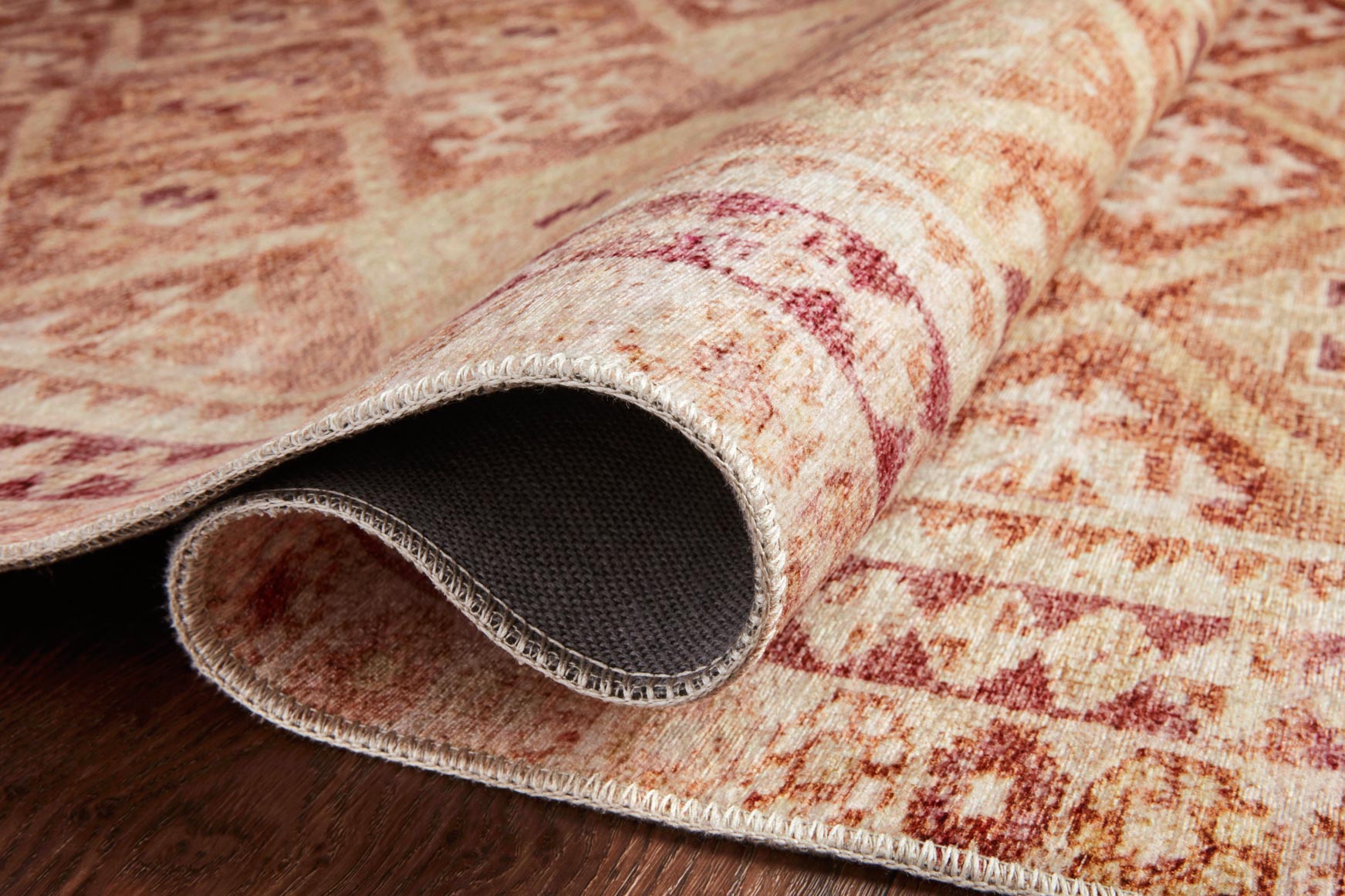 Close-up of rug pile and edge, natural beige with spice rust pattern and gray backing.