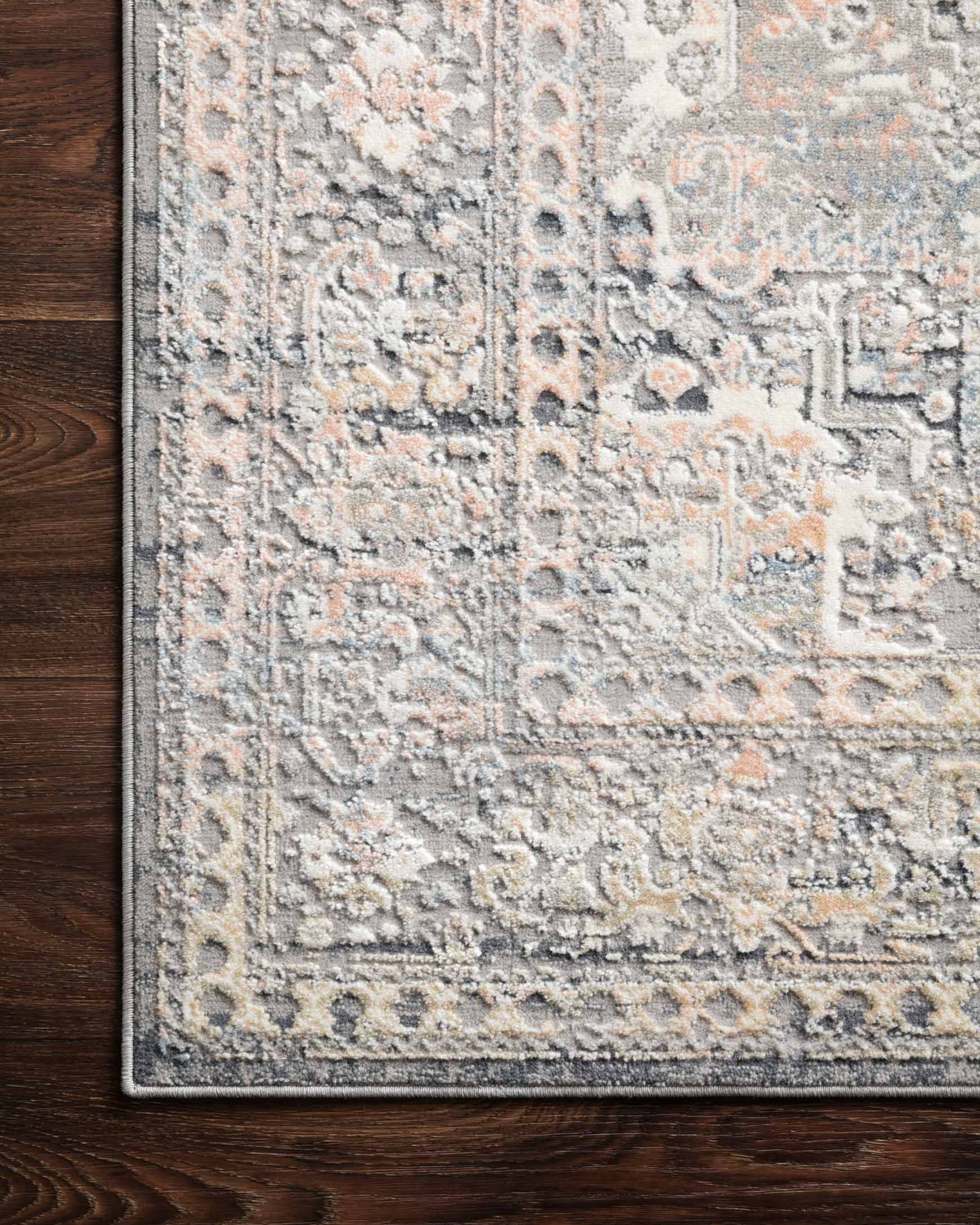 Textured close-up of light grey rug showing raised distressed motifs and stitched edge