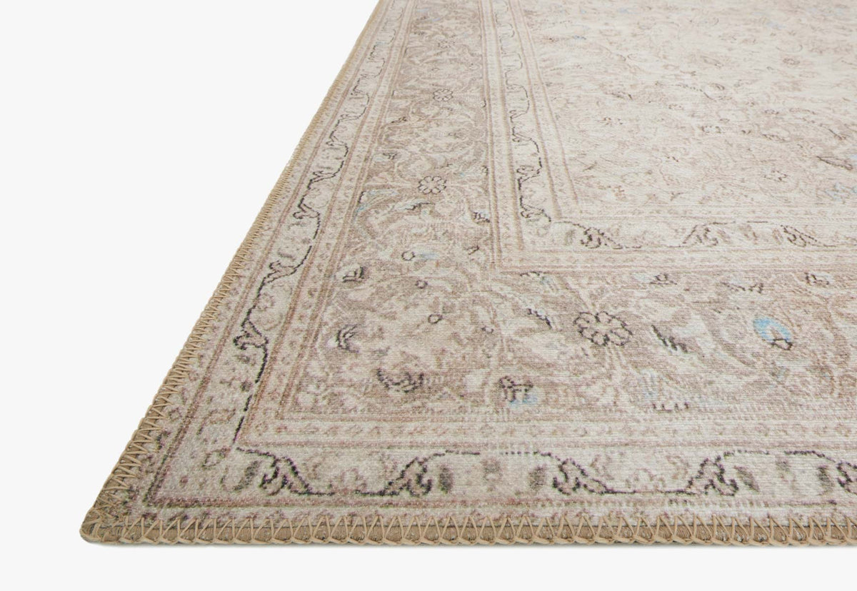 Corner view of sand and taupe rug with dense motifs and short fringed edge