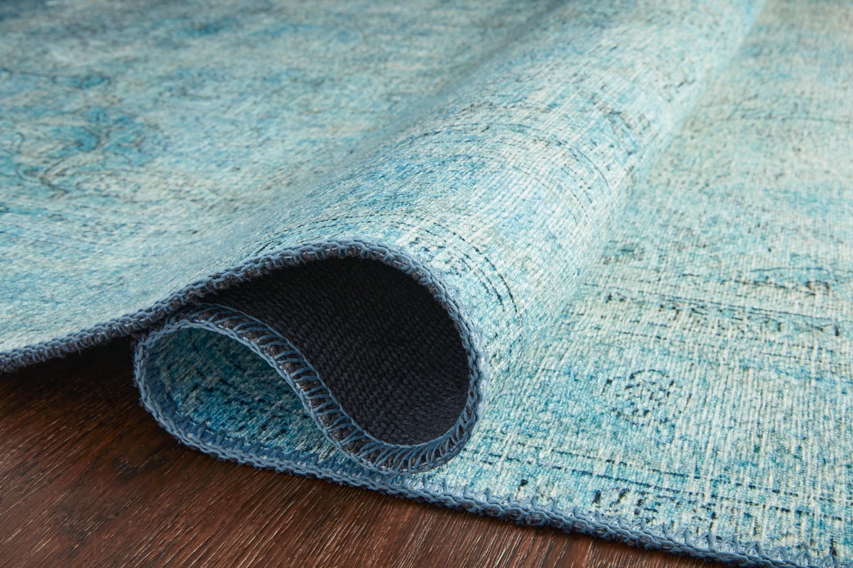 Rolled aqua rug with dark backing visible along the edge
