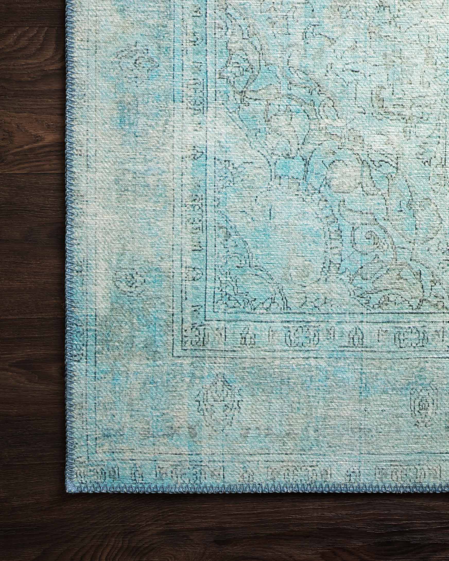 Aqua rug with ornate distressed motif and detailed border on woven surface