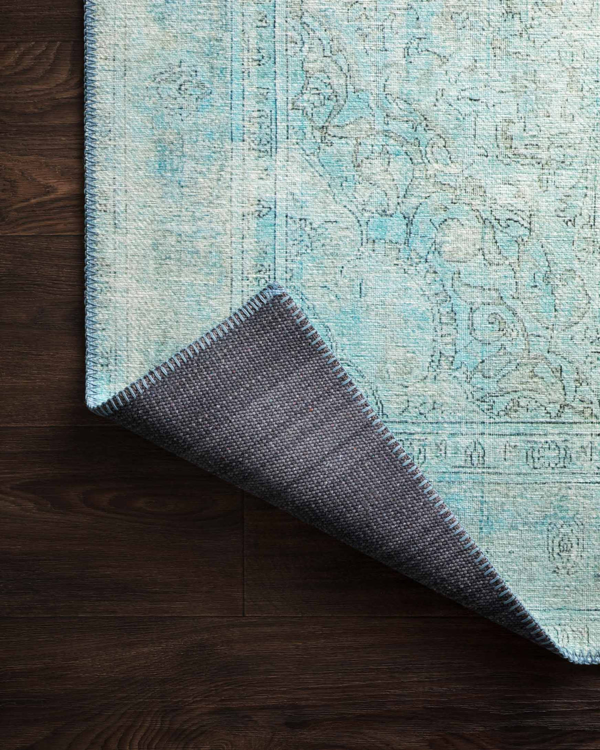 Aqua rug with folded corner and dark underside, stitched selvage edge