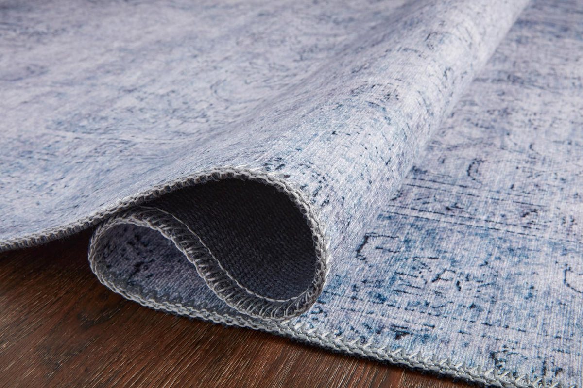 Slate blue rug edge with stitched border and visible underside backing