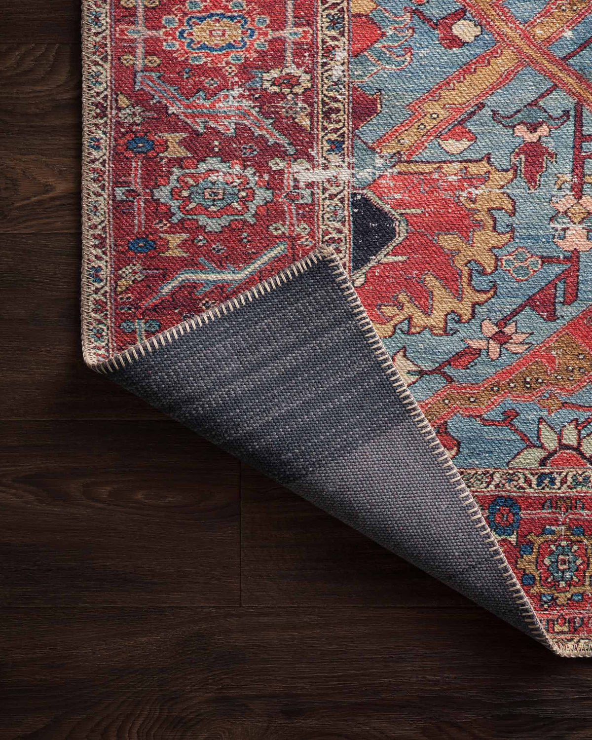 Corner fold of blue and red rug with underside fabric visible and stitched edge.