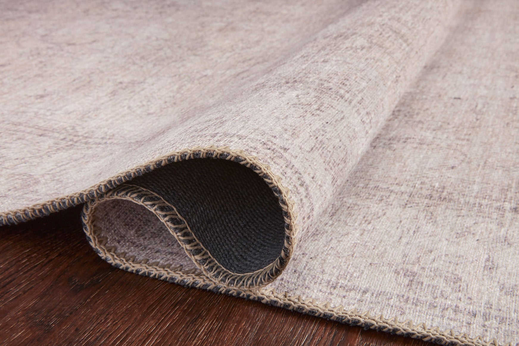 Sand rug corner showing thick low-pile texture and dark backing through edge