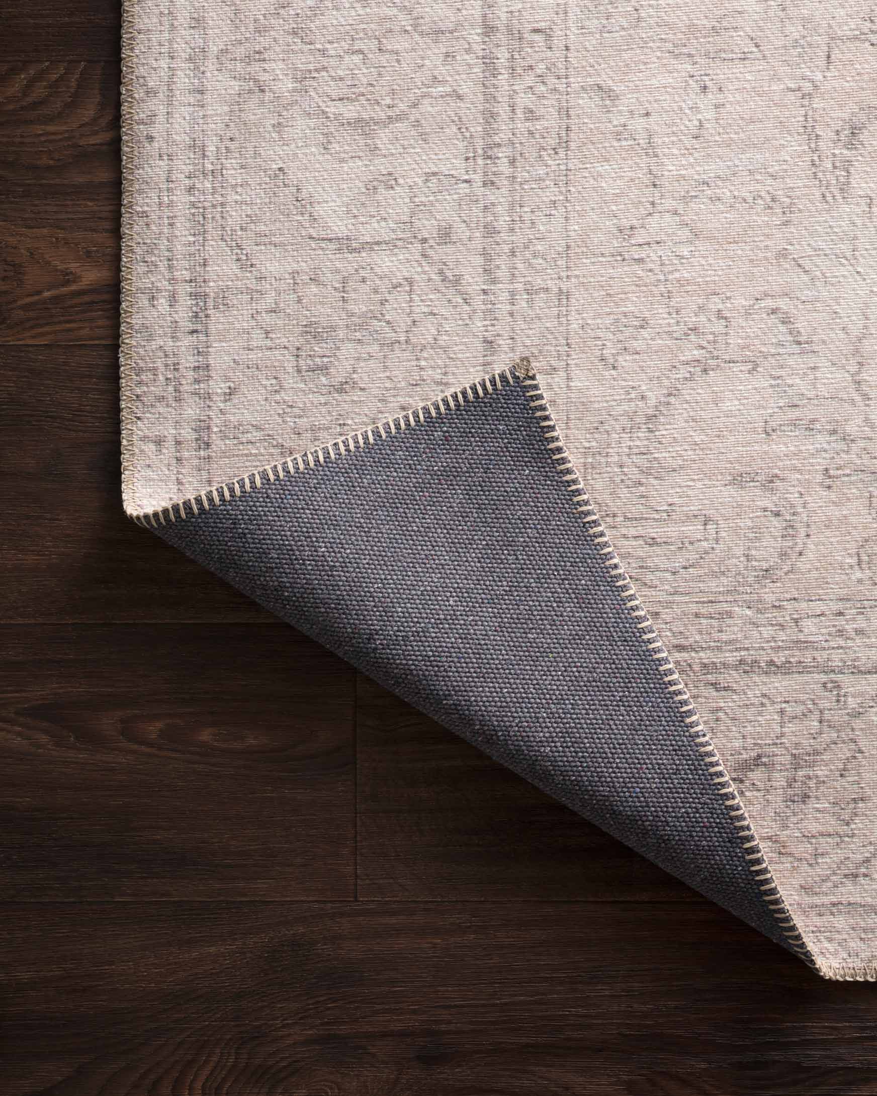 Rug corner detail with dark underside and light stitched edge on wood floor