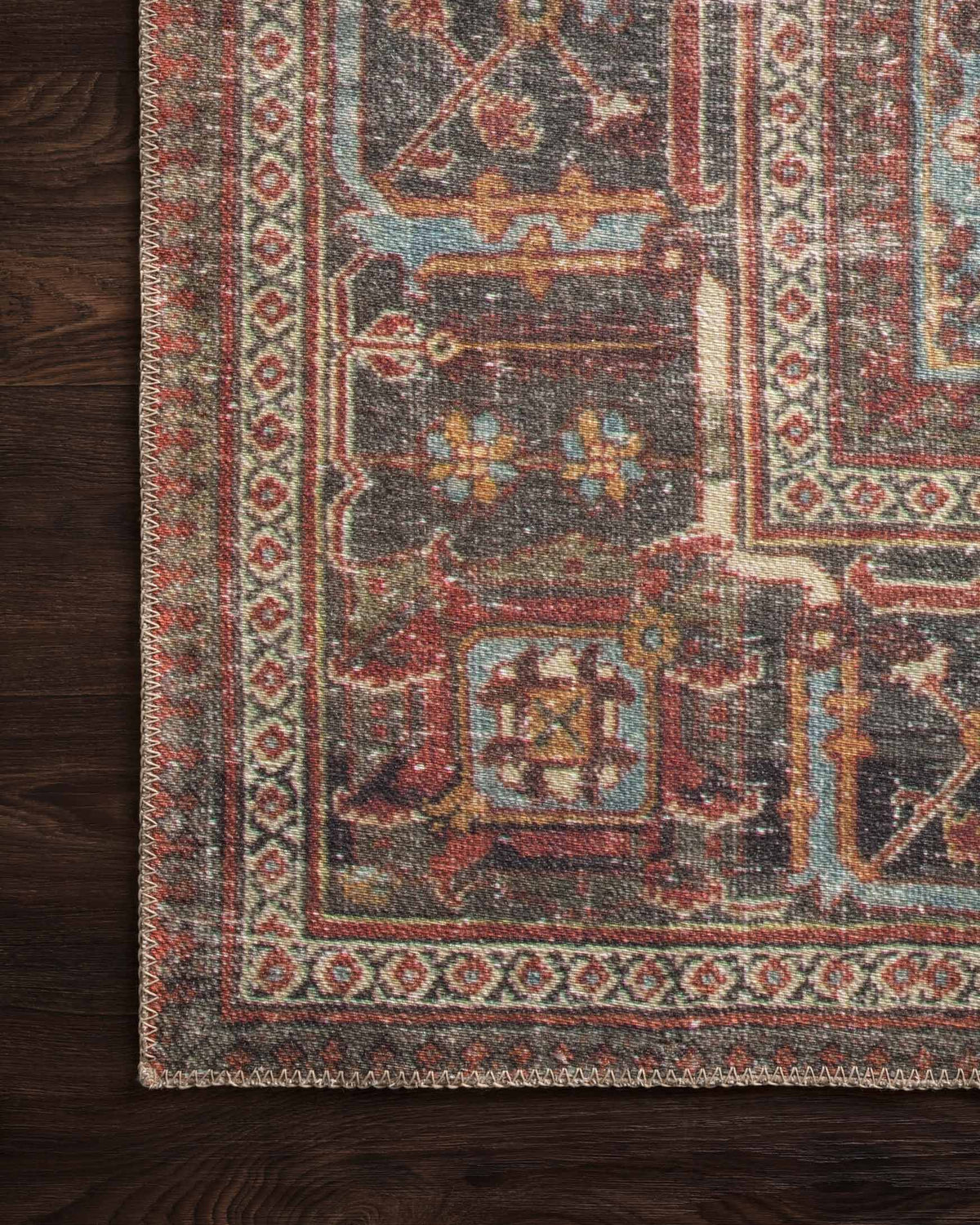 Close-up rug corner with multicolor geometric border on dark wood floor.