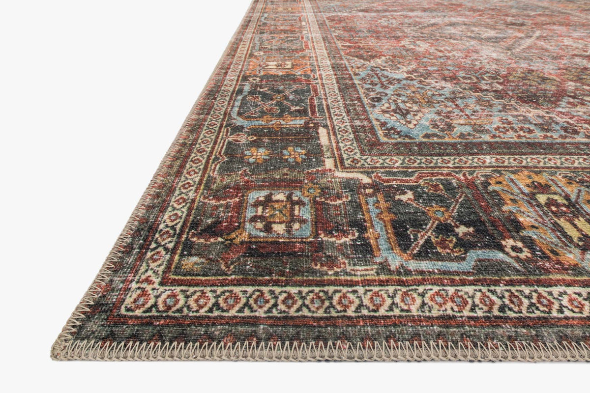Corner detail of brick, teal, and dark navy patterned rug with border motifs.