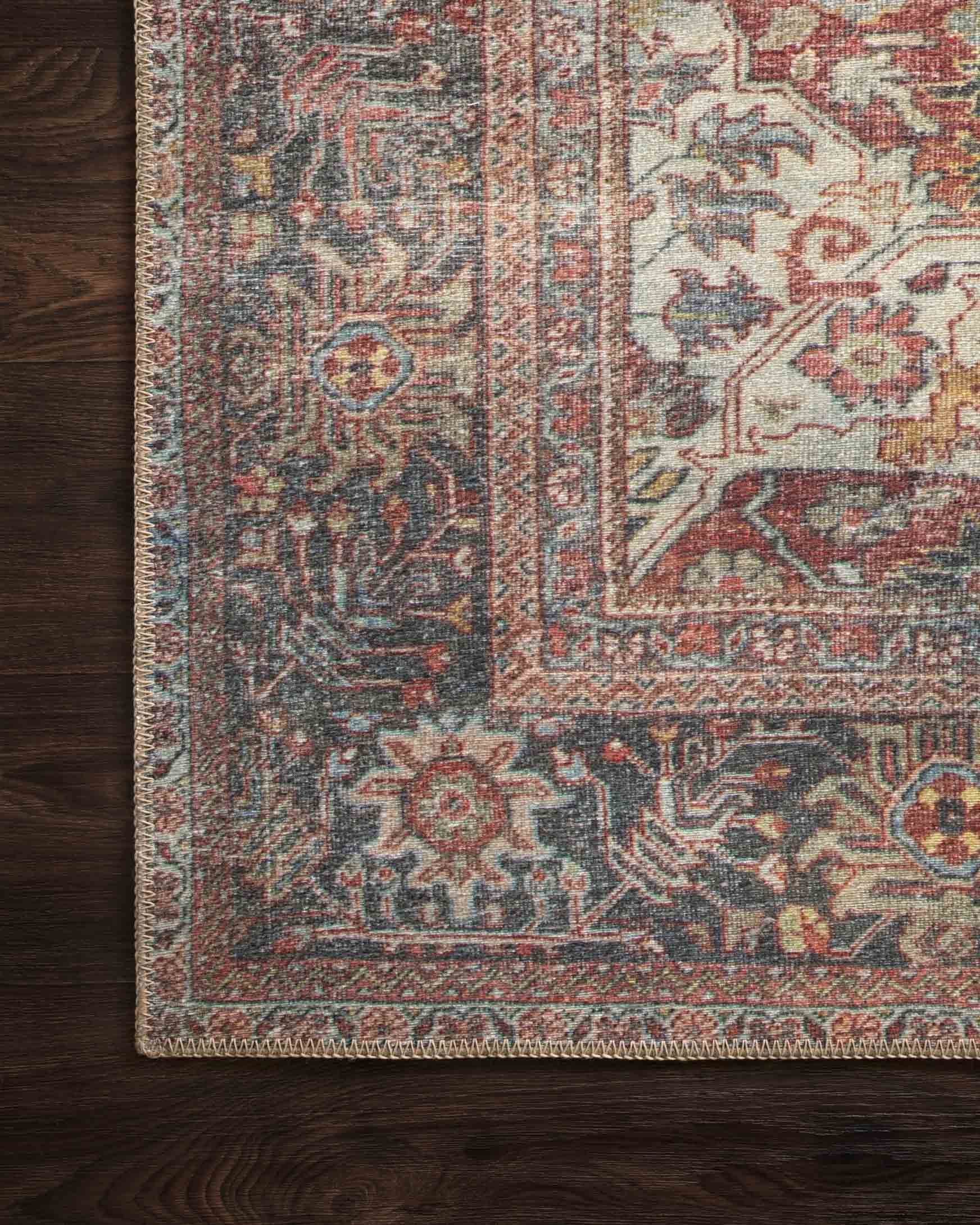 Rug corner on dark wood floor, showing ornamental border and medallion in brick and blue.