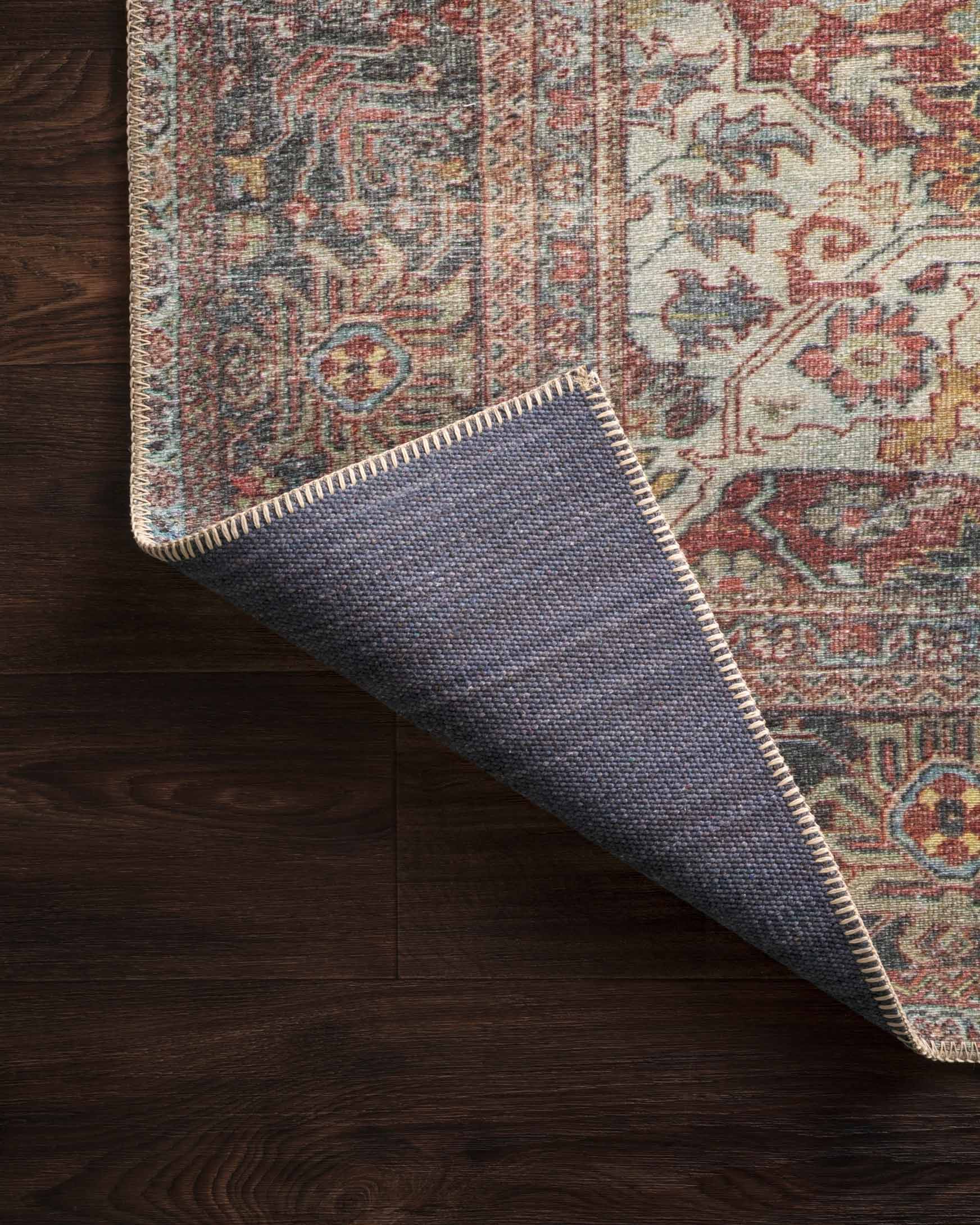 Rolled rug corner with bound edge, traditional pattern in brick, blue, and cream tones.