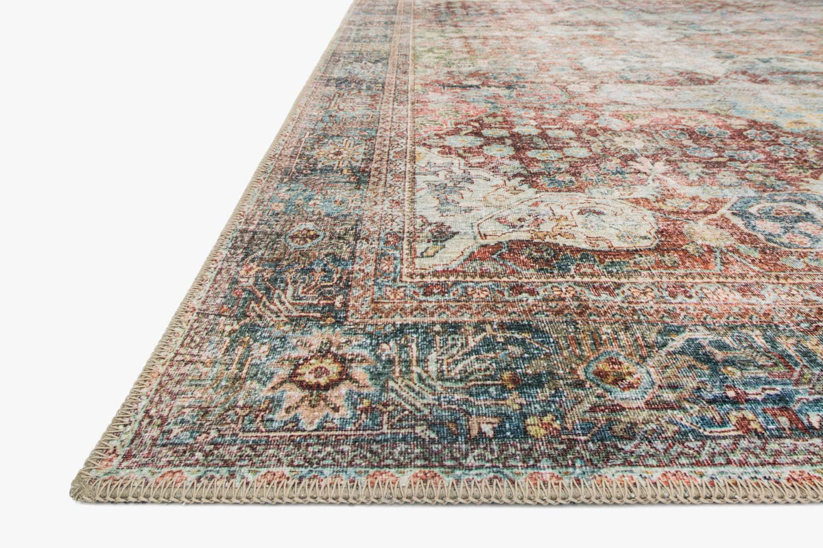 Rug corner with fringed edge, traditional pattern in brick, blue, and cream on light ground.
