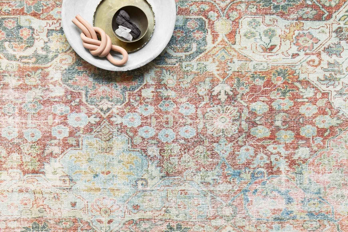 Close-up of traditional rug pattern with red-brick, blue, and cream motifs and border details.