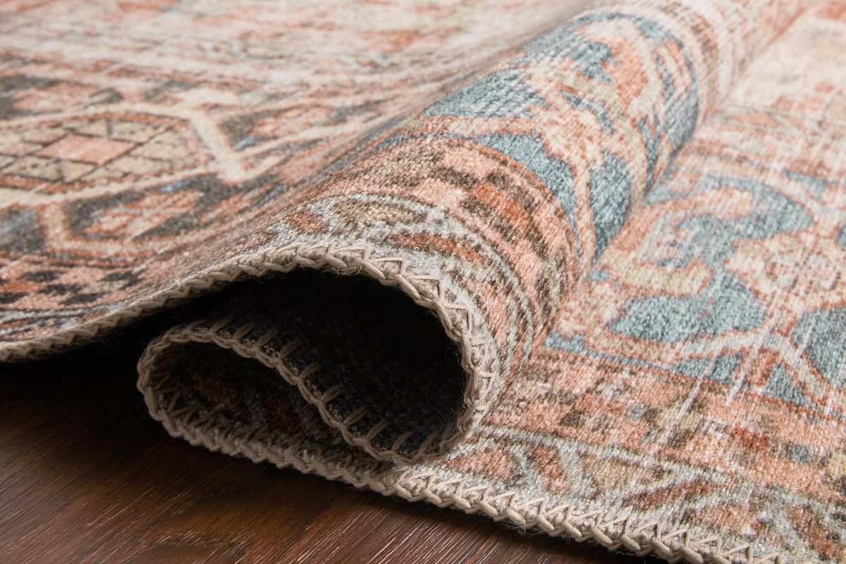 Rolled rug corner with braided fringe, showing terracotta and blue woven pattern.