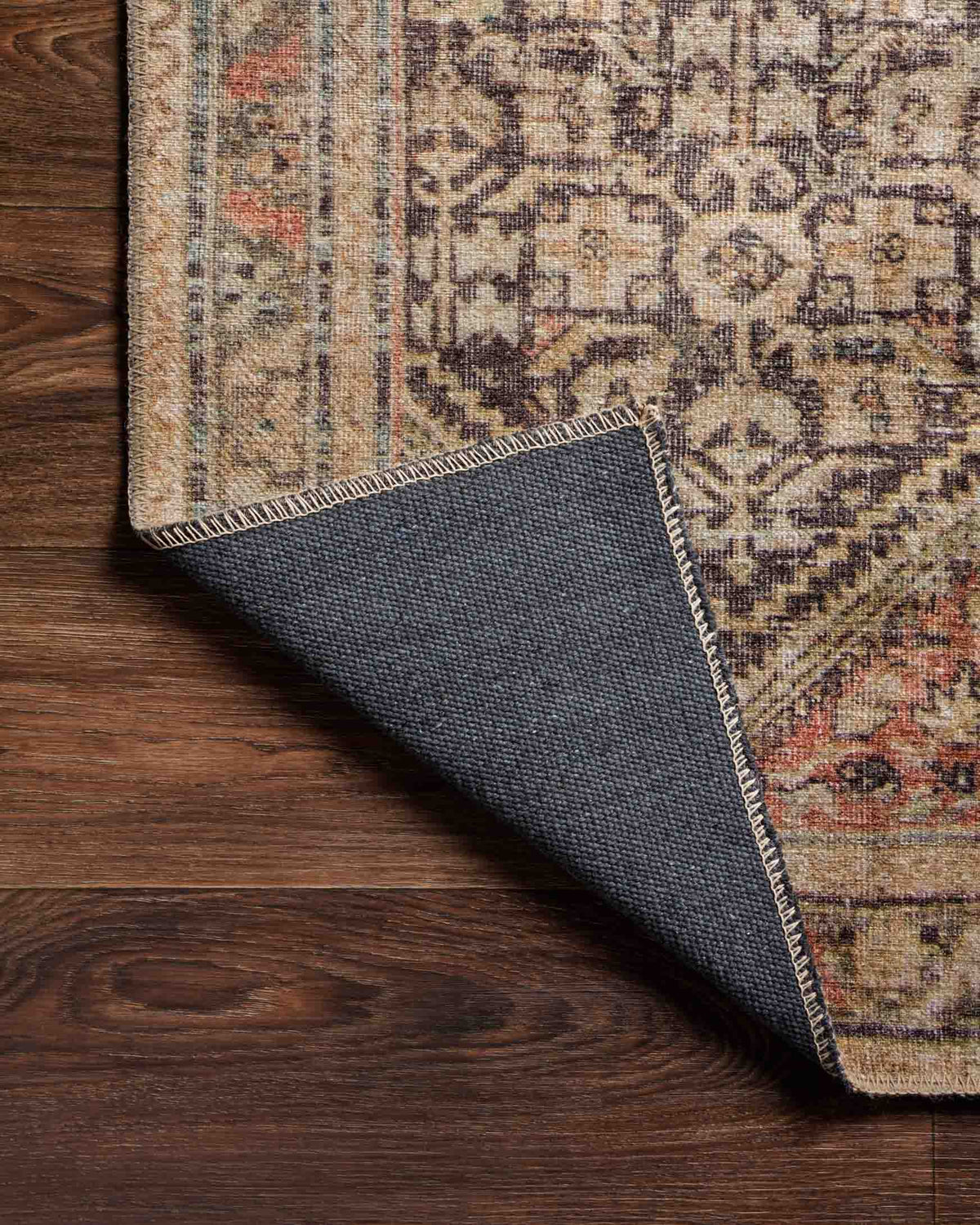 Corner close-up showing rug edge binding and dark backing on a charcoal patterned base