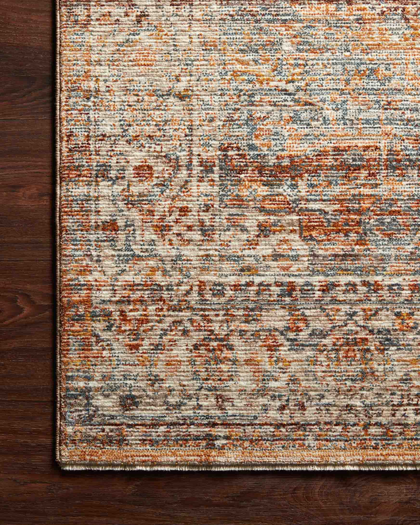 Rug corner on dark wood floor: cream with orange and blue mottled pattern.
