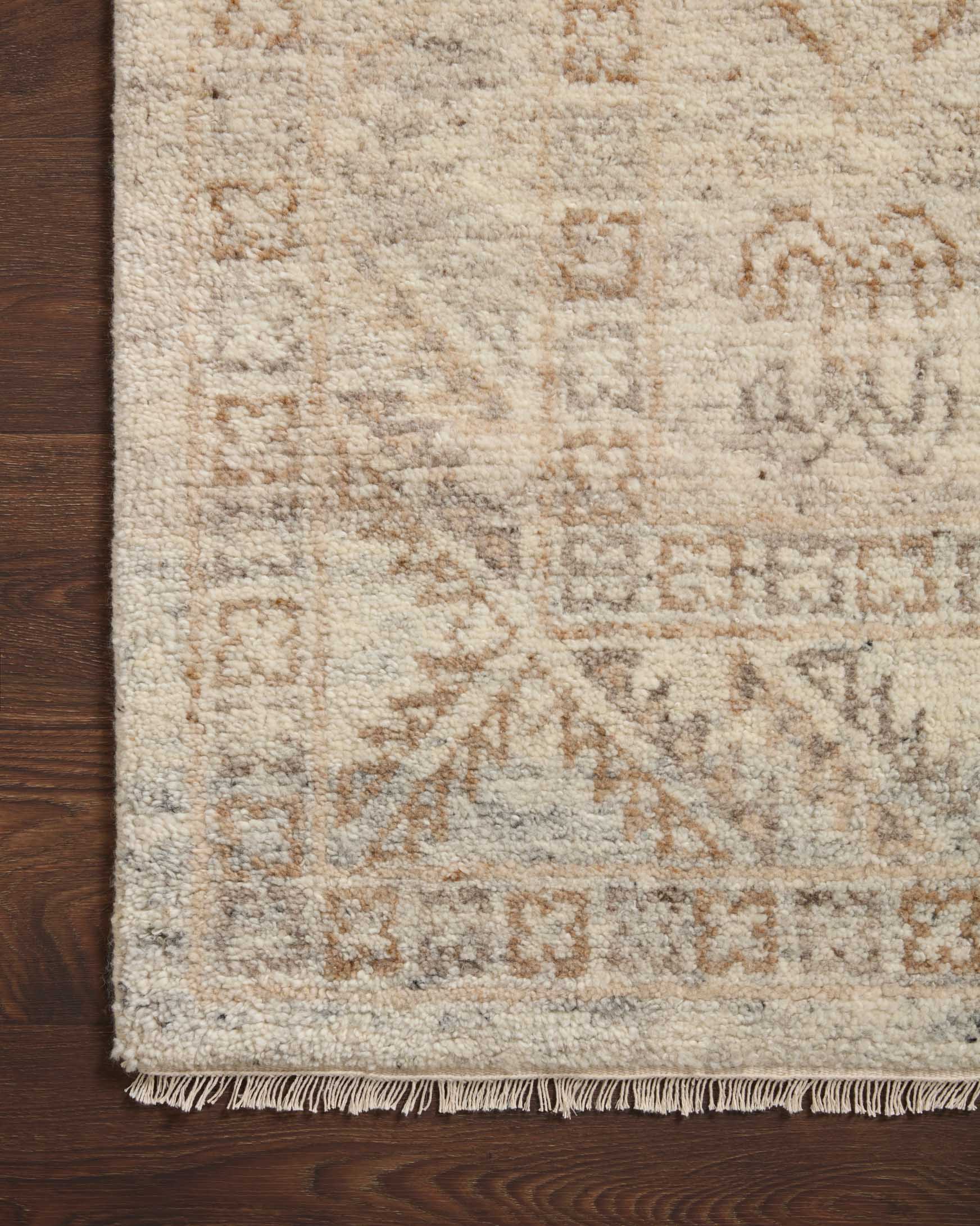 Corner of natural and mocha woven rug with dense faded pattern and fringed edge.