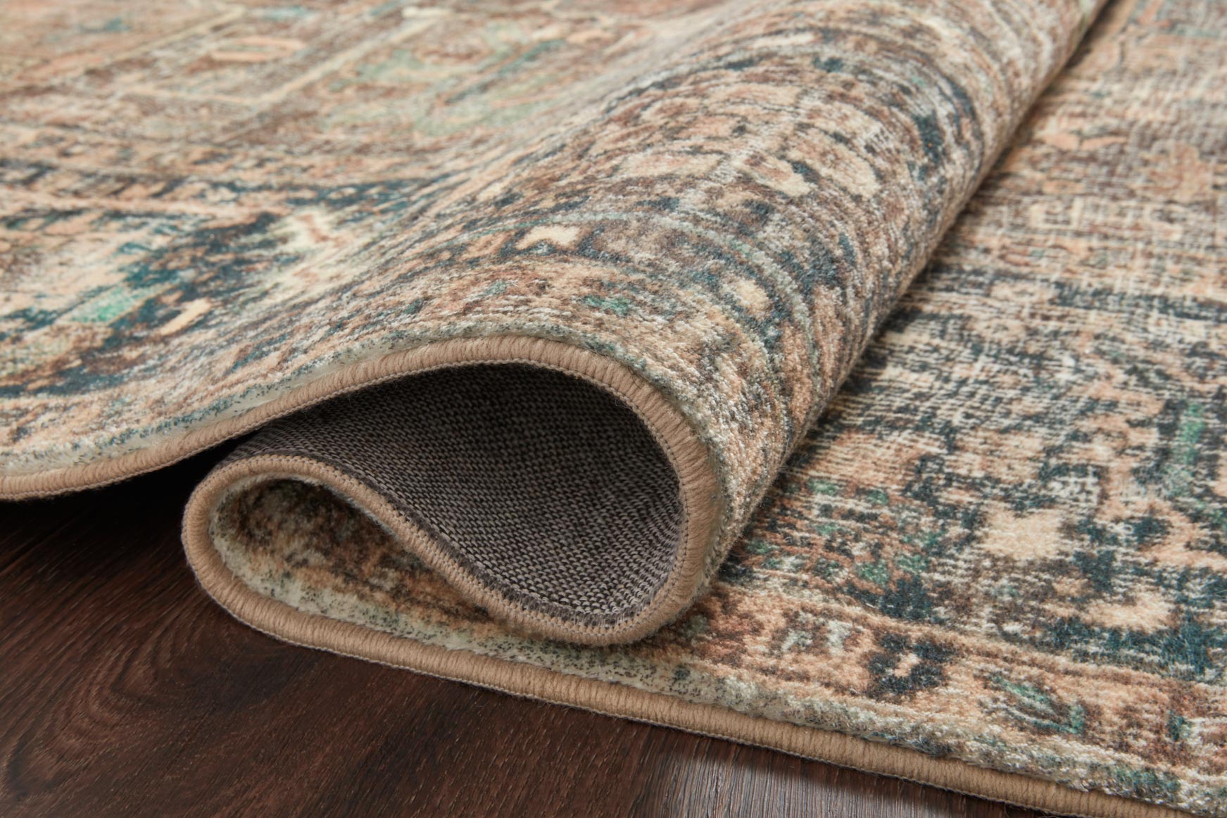 Rolled edge of traditional rug showing low-pile texture in blue, teal, and cream tones