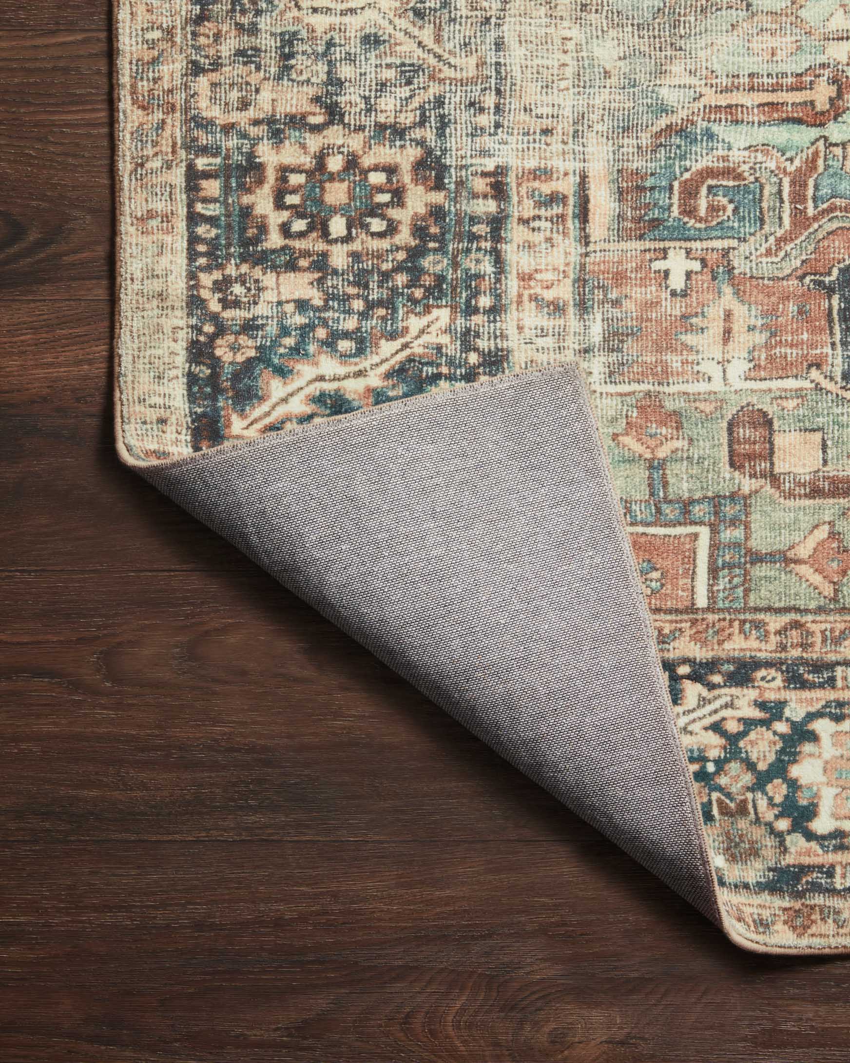 Rug corner detail with blue and teal motifs and light border; gray backing visible