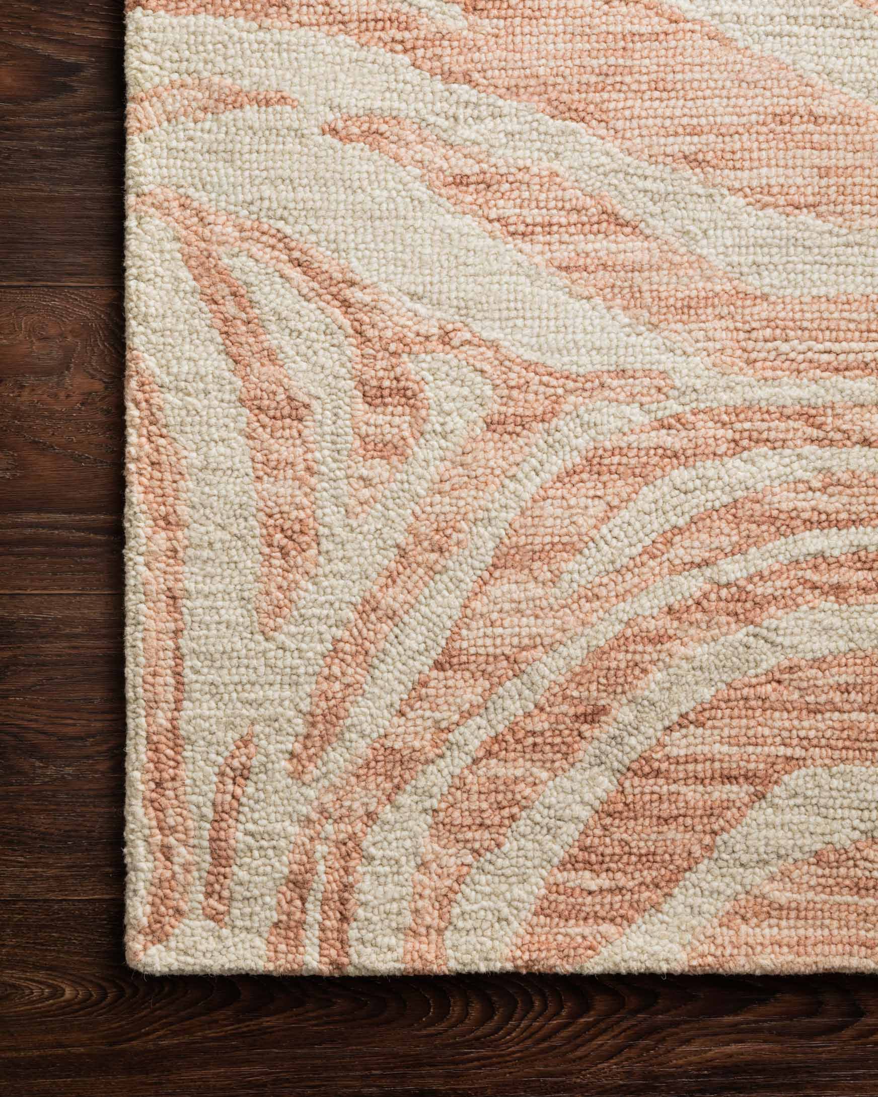 Hooked rug corner with blush and ivory abstract curves, textured looped pile.