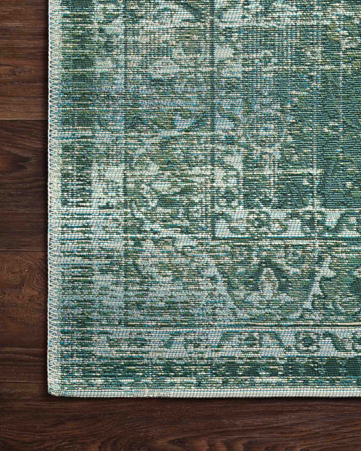 Corner view of green and mist patterned area rug with flat border and woven texture