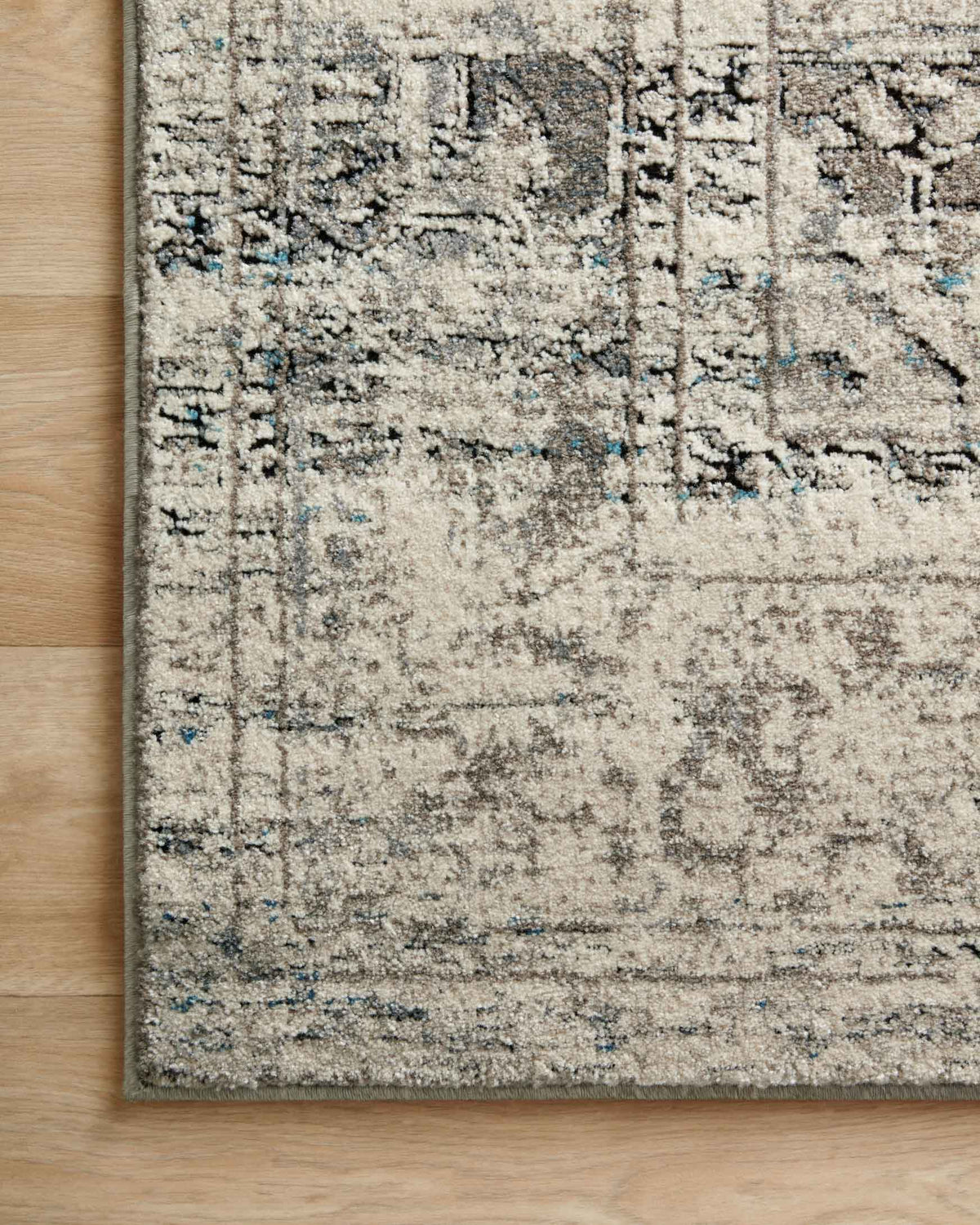 Taupe and ivory rug with geometric distressing and muted blue flecks near border