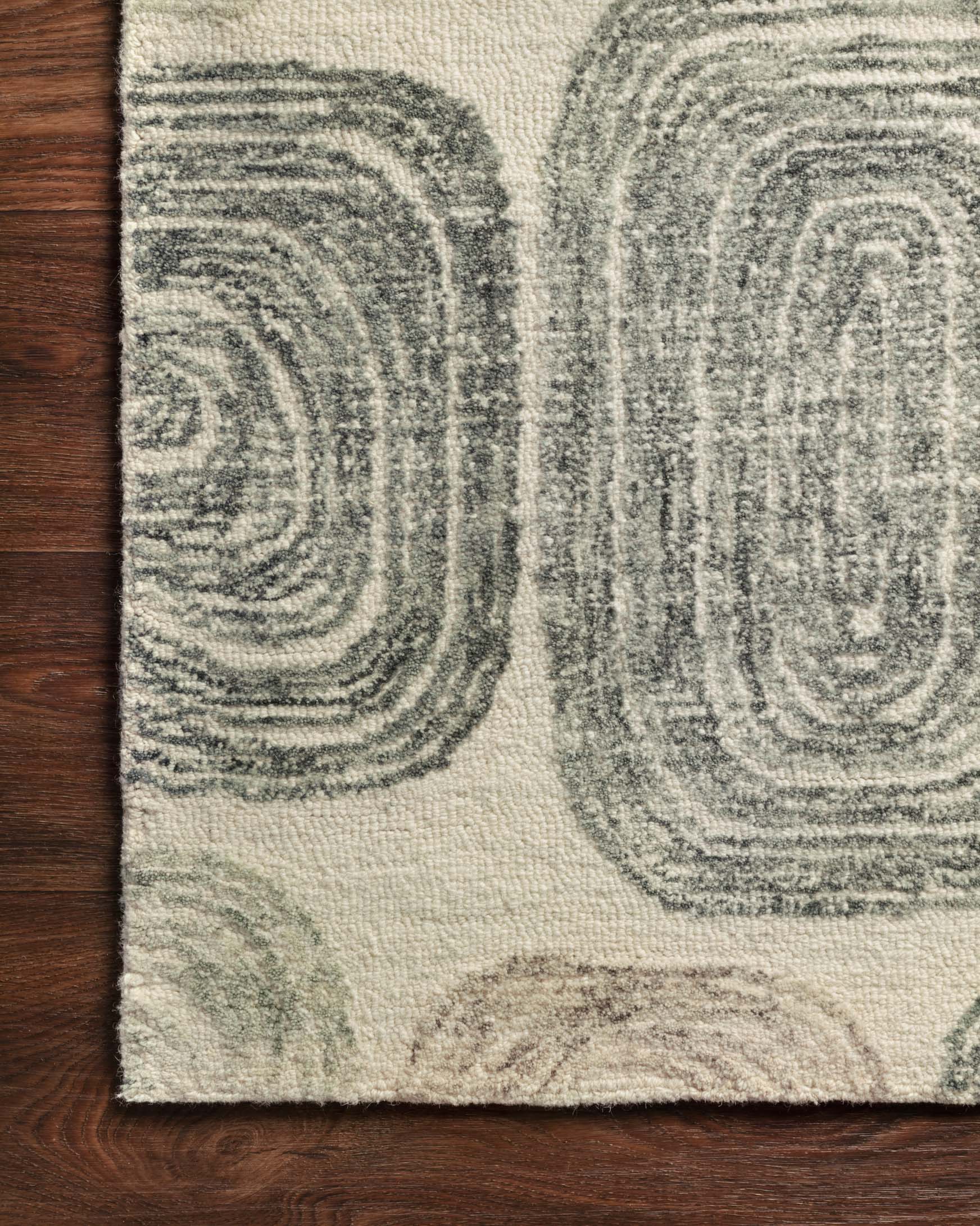 Hand-tufted rug close-up with layered swirl motifs in dark gray, neutral background