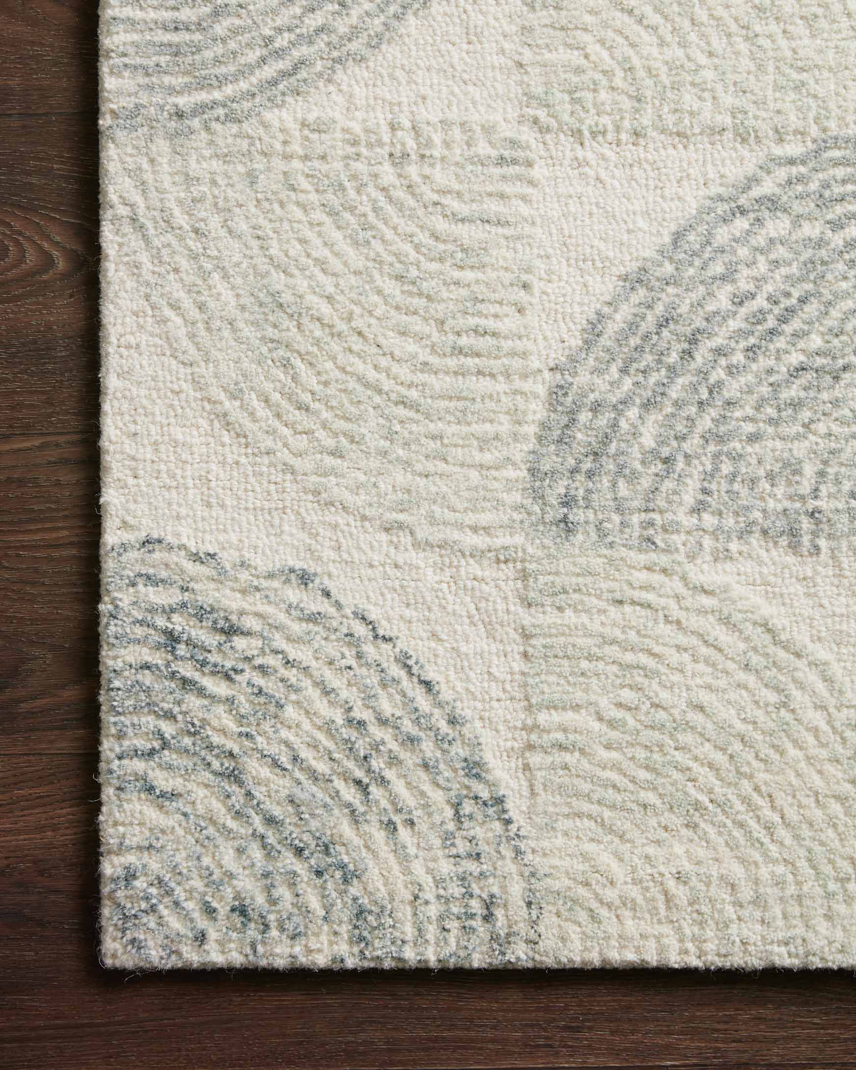 Hand-tufted rug close-up: cream pile with slate-blue circle motifs near the edge