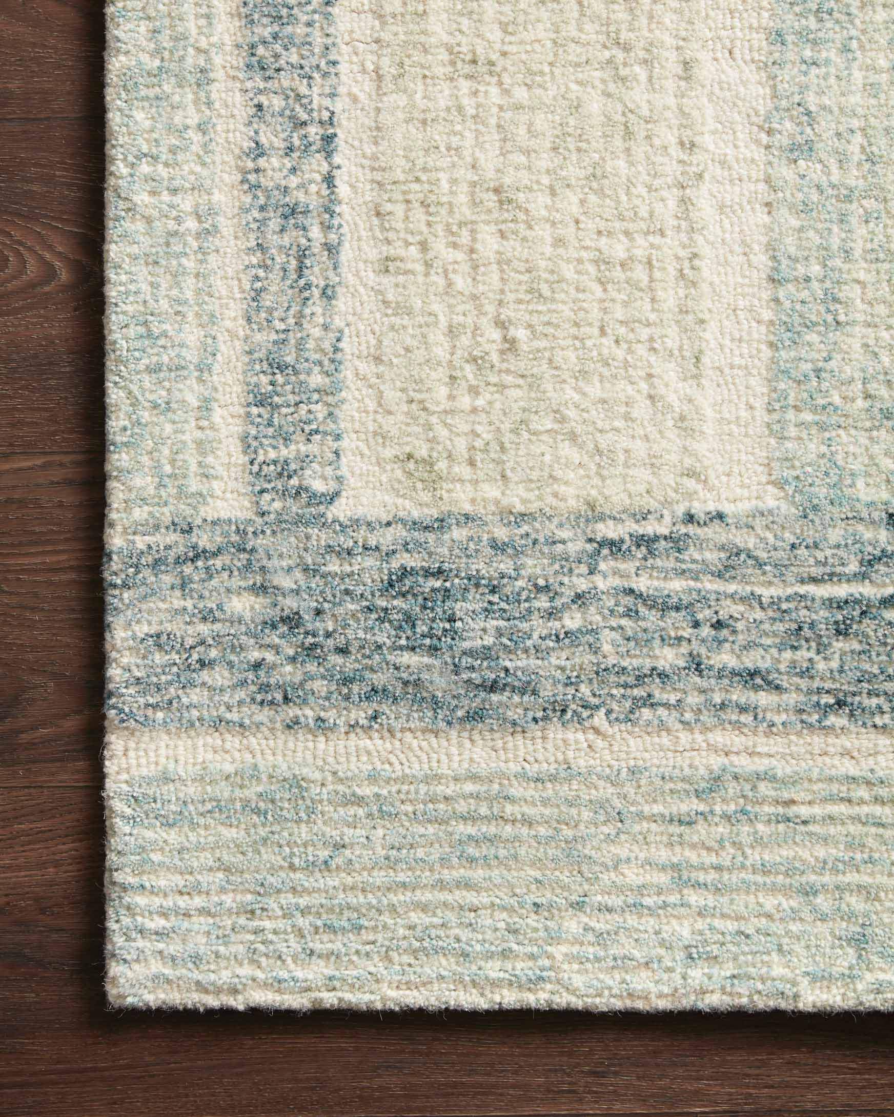 Close-up of aqua-and-denim abstract border on cream hand-tufted rug with textured pile