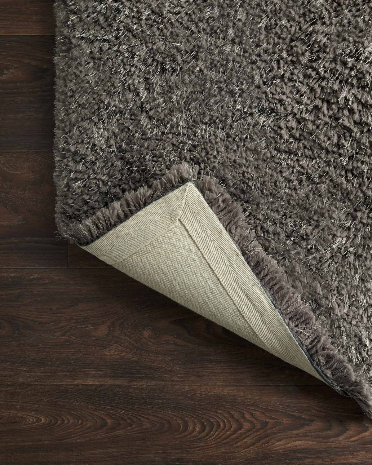 Charcoal shag rug corner showing woven backing and long fibers