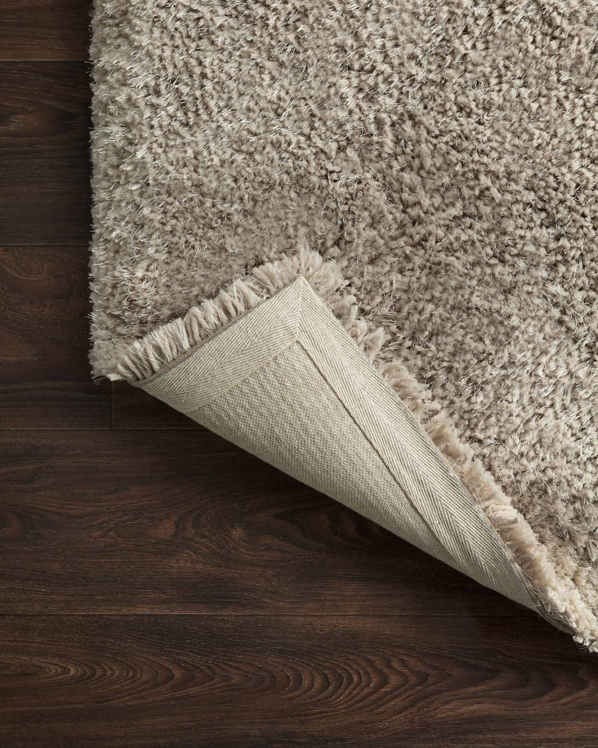 Grey shag rug corner with visible woven backing and bound edge.