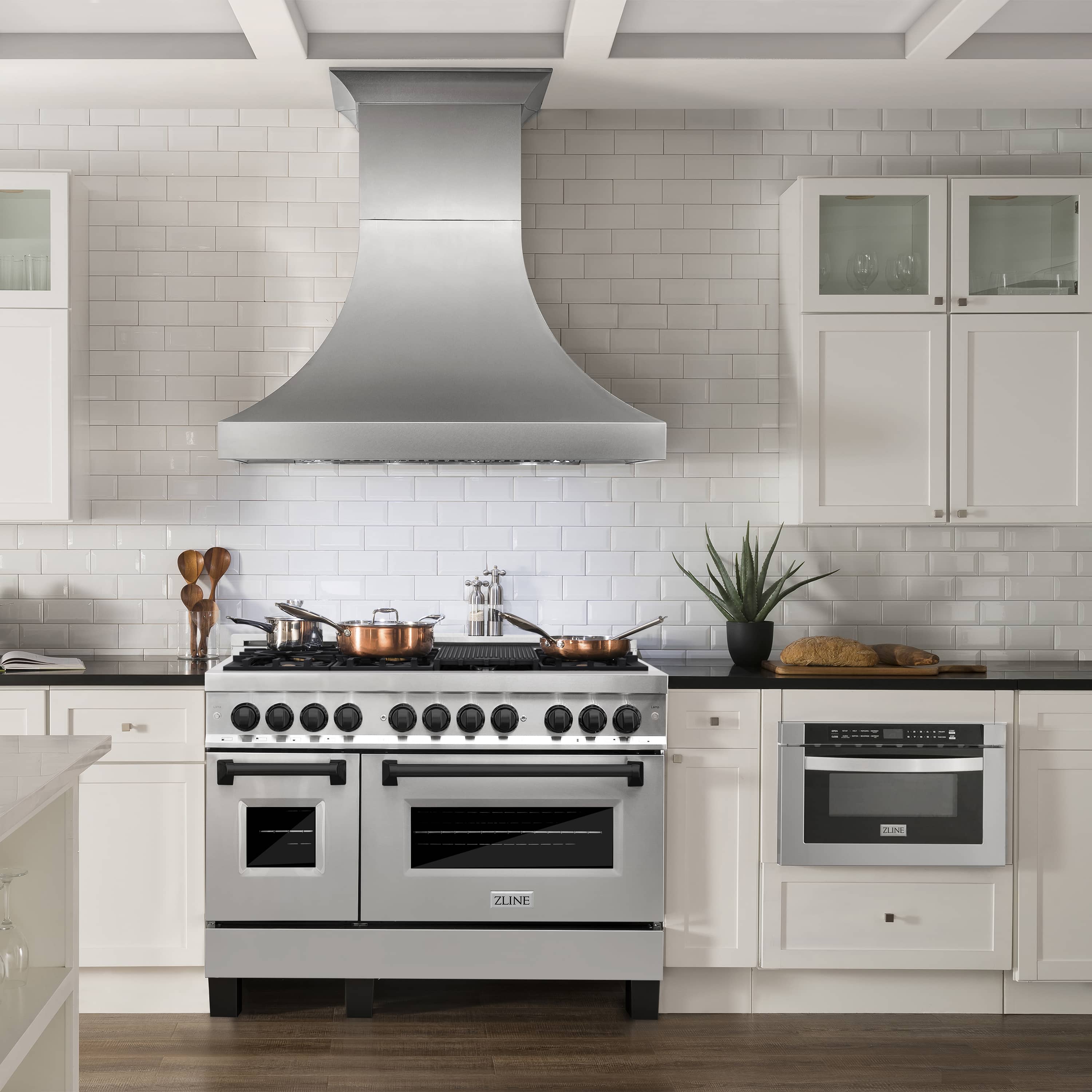 Front view of stainless steel dual fuel range with matte black knobs and overhead vent hood