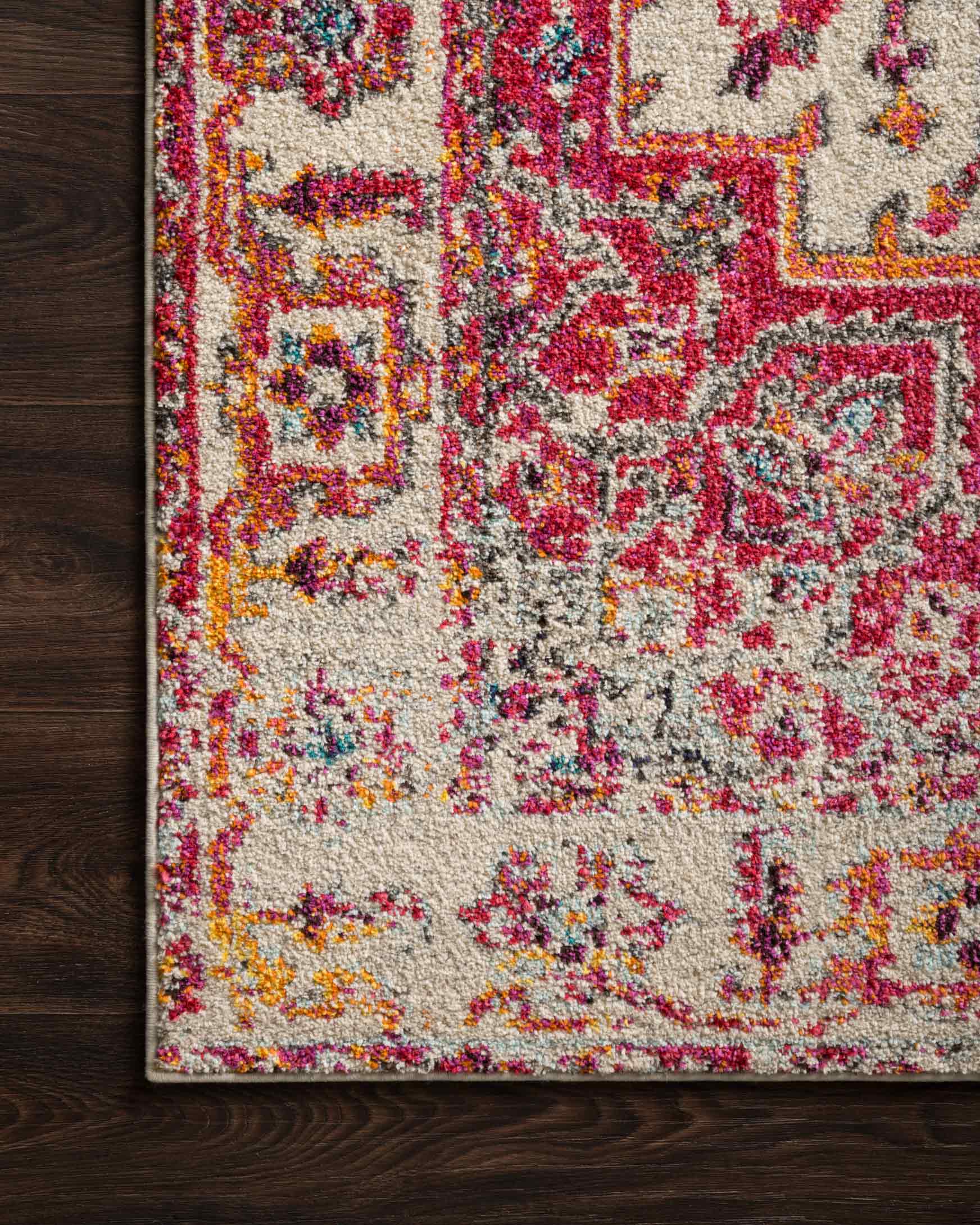Power-loomed rug corner on dark wood floor, ivory with pink, red, and blue ornamental design