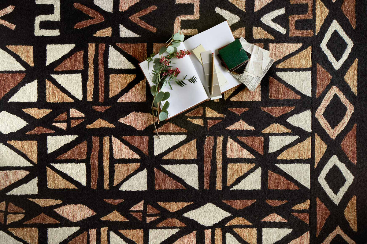Hand-tufted rug close-up with geometric star and arrow pattern in spice, black, and cream.