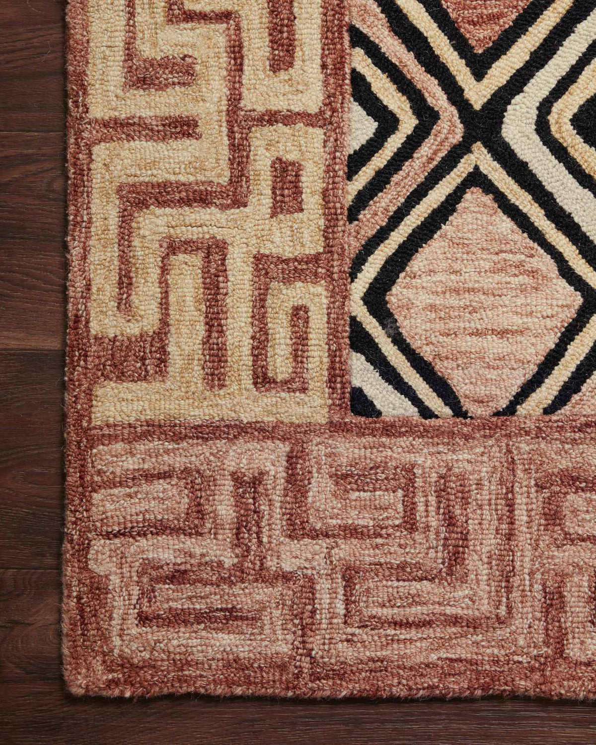 Corner detail of rose and black hand-tufted rug with geometric diamond motif