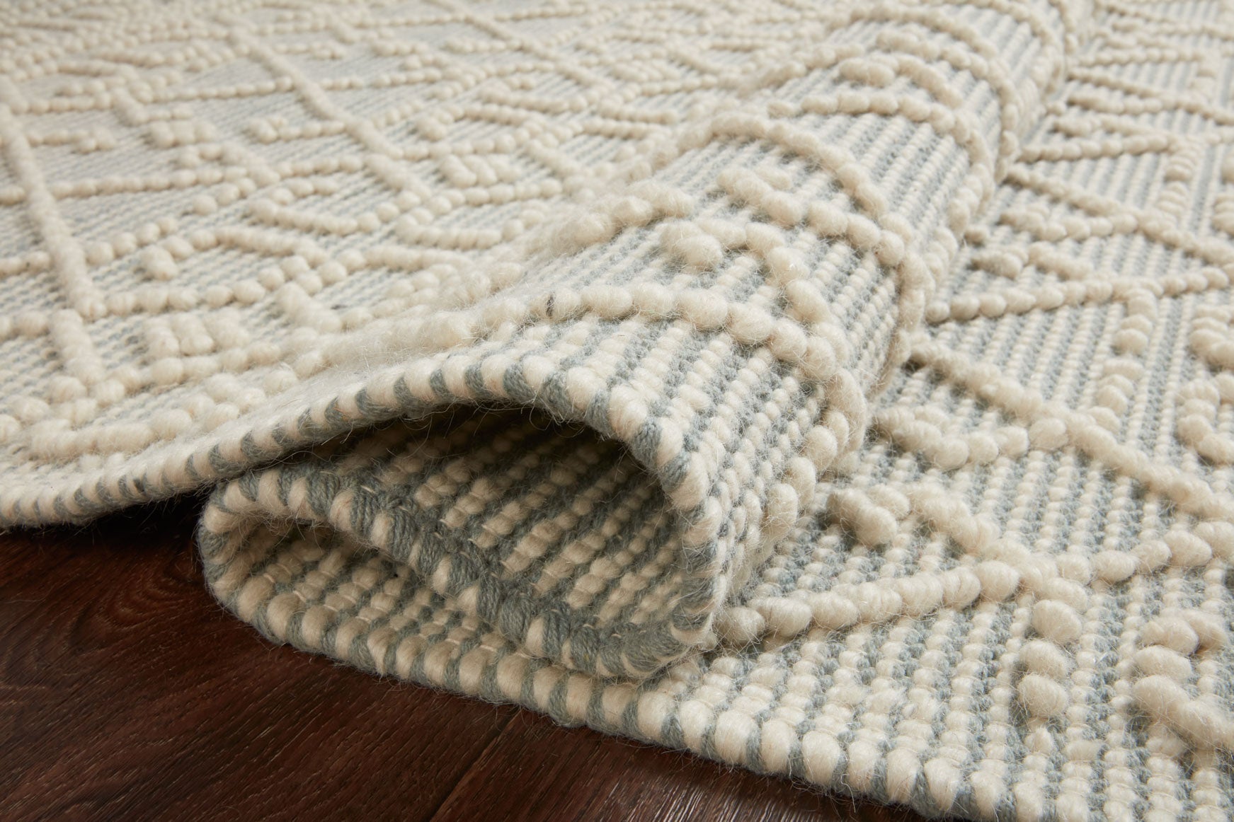 Ivory and blue geometric rug showing rolled edge, thick pile, and woven texture