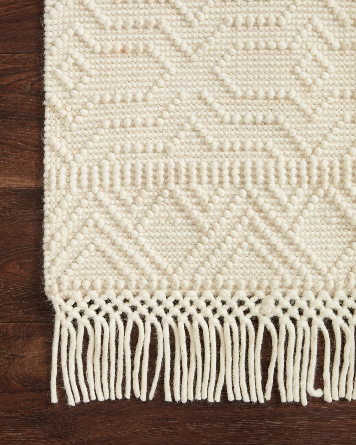 Ivory rug close-up with raised geometric weave and long fringe along the edge