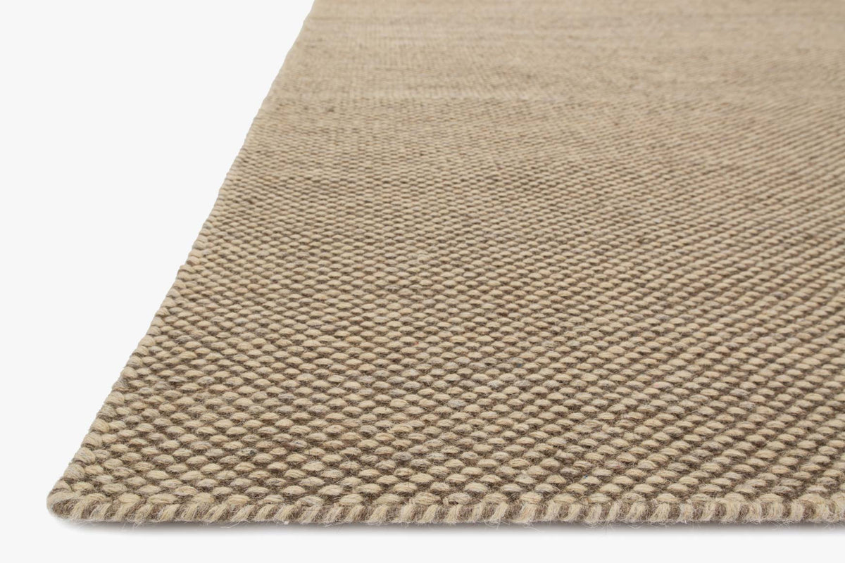 Natural hand-woven rug corner detail with braided fringe and textured weave.
