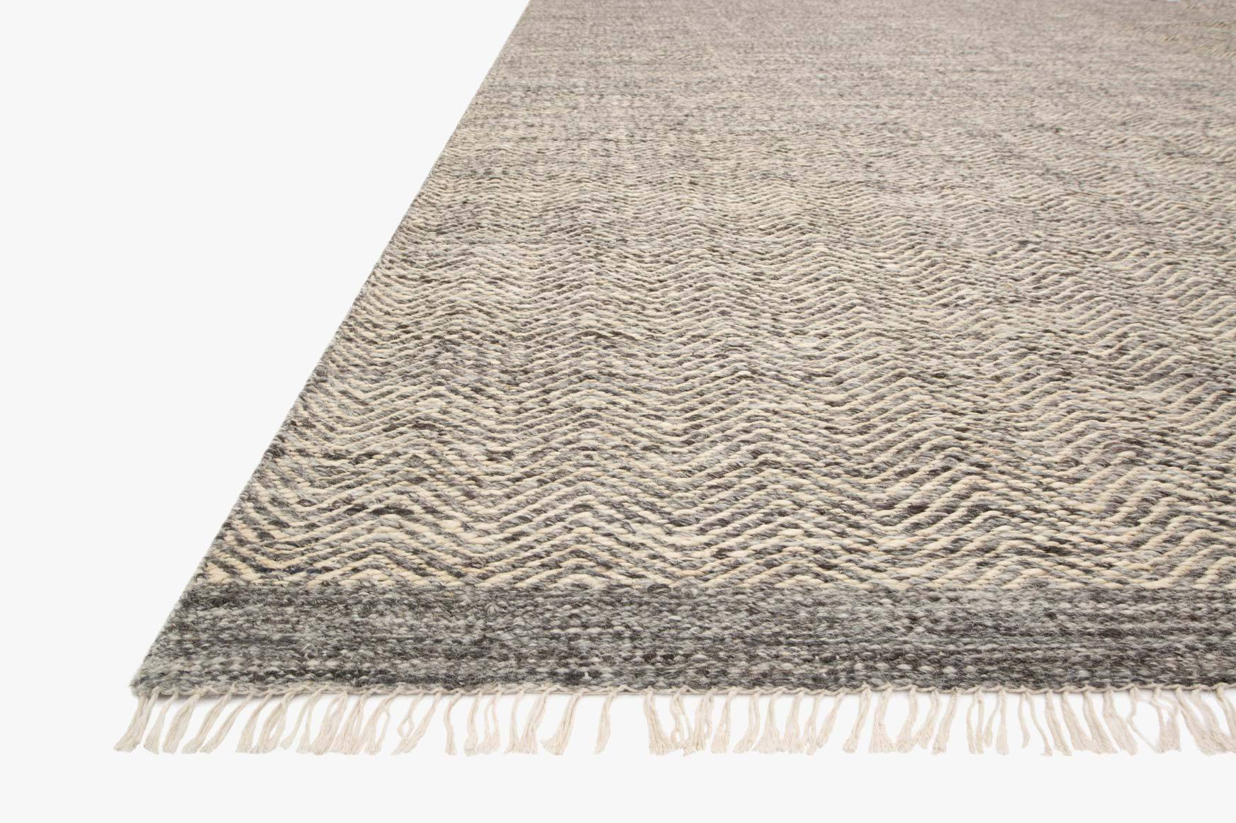 Grey hand-woven rug corner showing zigzag weave and off-white fringe on the edge.