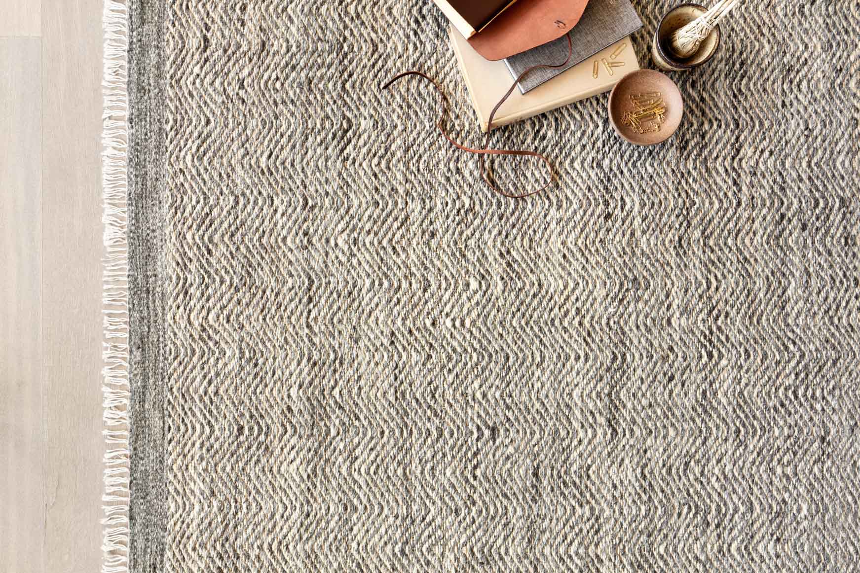 Grey hand-woven rug close-up with wavy zigzag texture and light fringe edge.