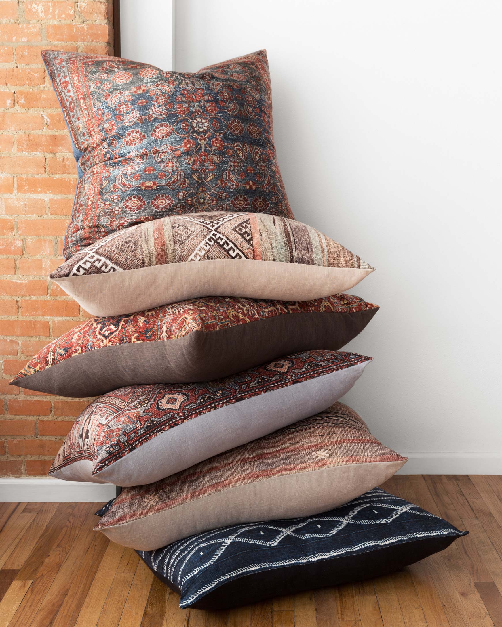 Stack of decorative pillows with patterned multi-color covers and beige solid backs