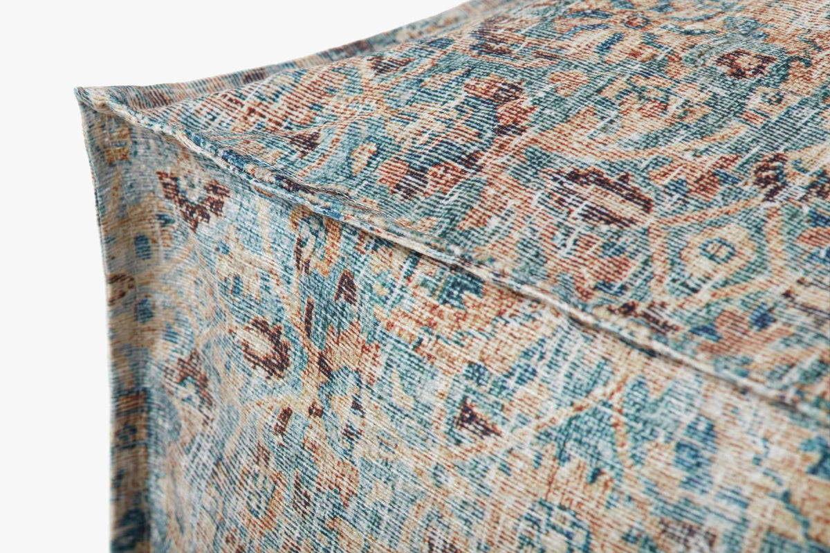 Corner view of geometric-pattern woven pouf in blue and tan with orange accents.